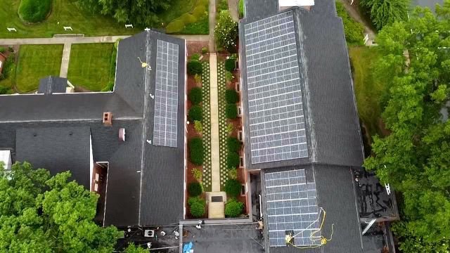 An aerial view of two adjacent buildings with solar panels on their roofs. A walkway with trees and benches runs between the buildings.