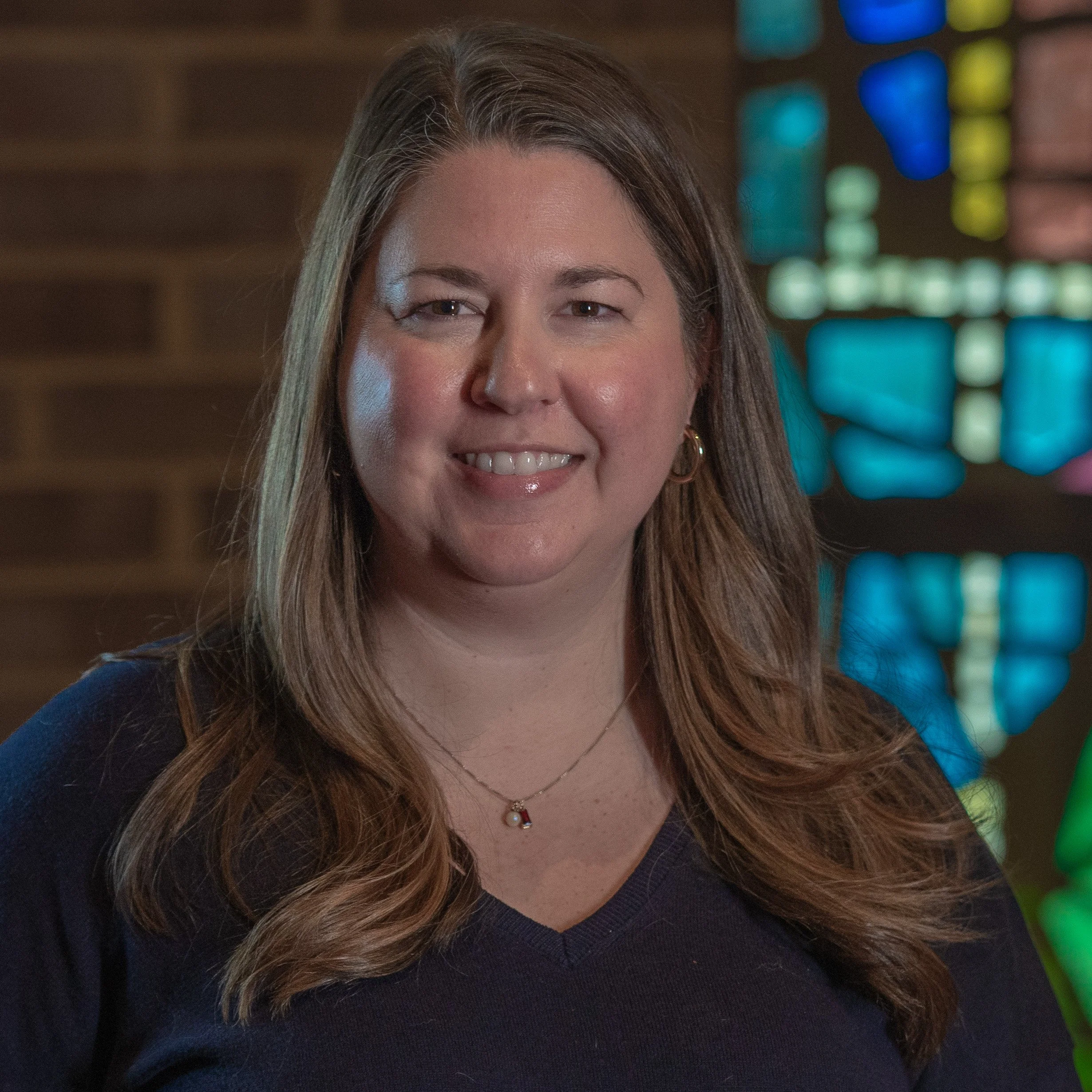 Woman smiling indoors with stained glass background.