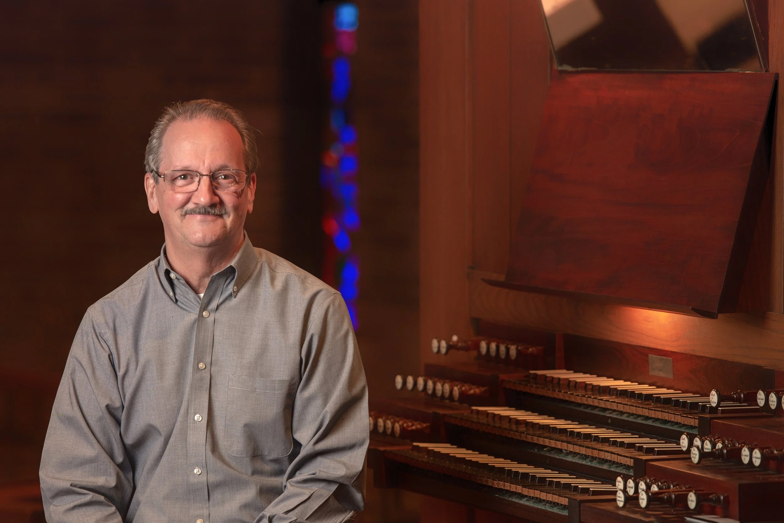 Man smiling next to a large pipe organ in a church setting.