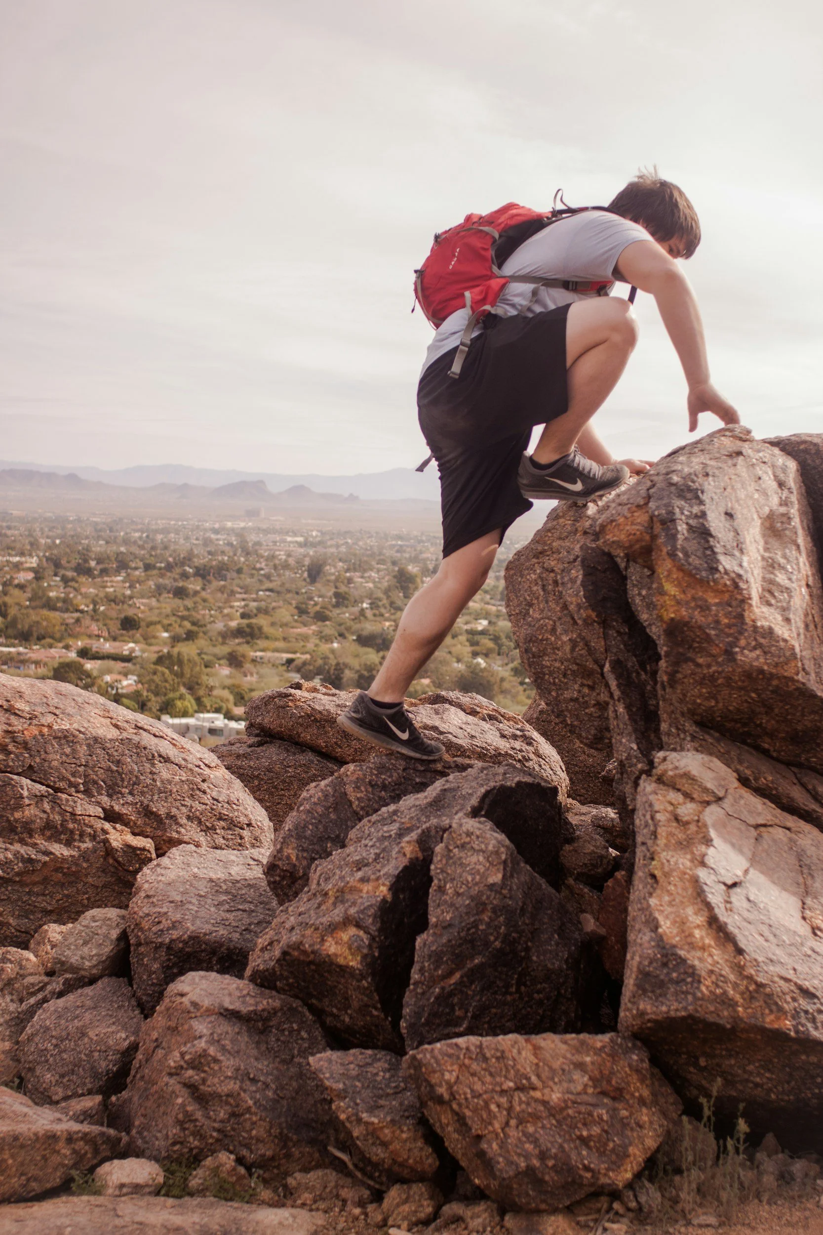 Person climbing rocks with a red backpack in a mountainous area. arkansas hike, rentals