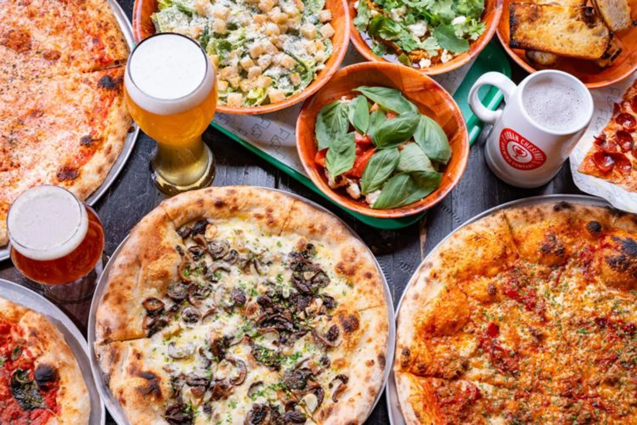Overhead shot of pizzas, salads, and beer