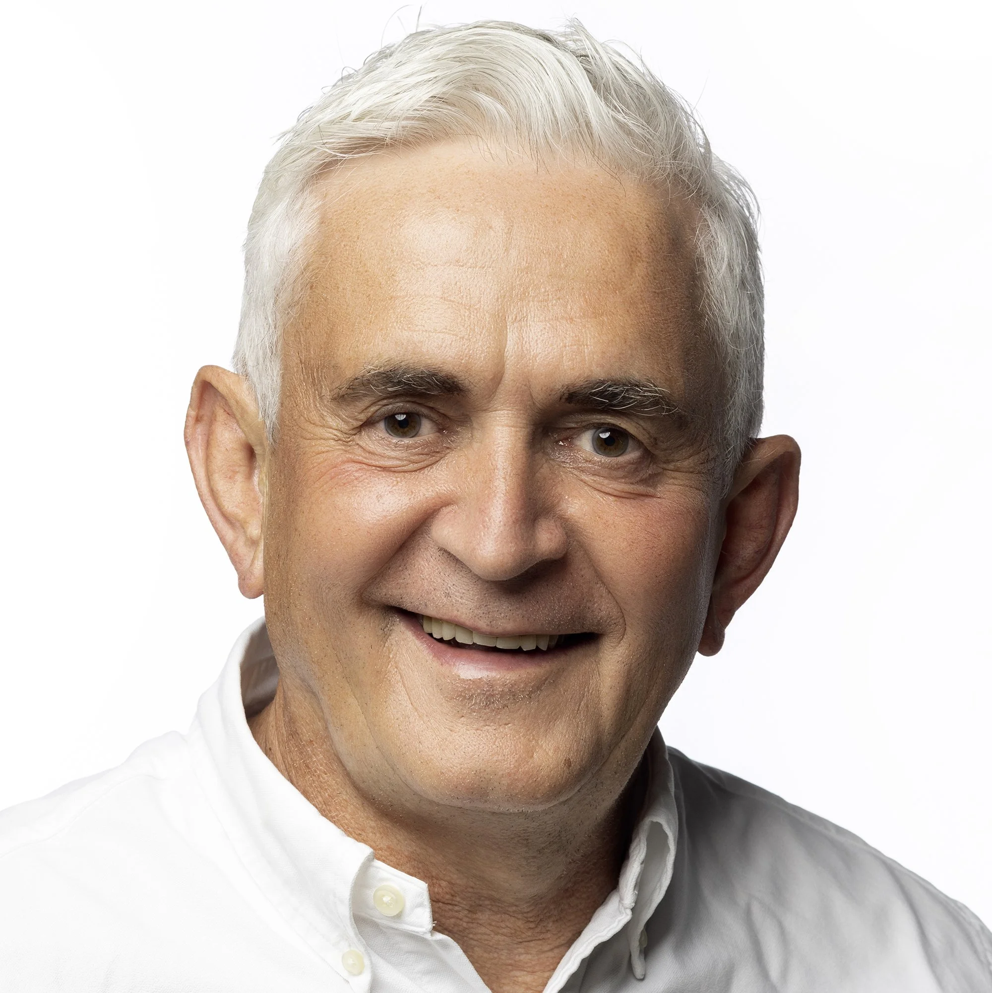 Close-up of a middle-aged man with gray hair wearing a white button-down shirt, smiling.
