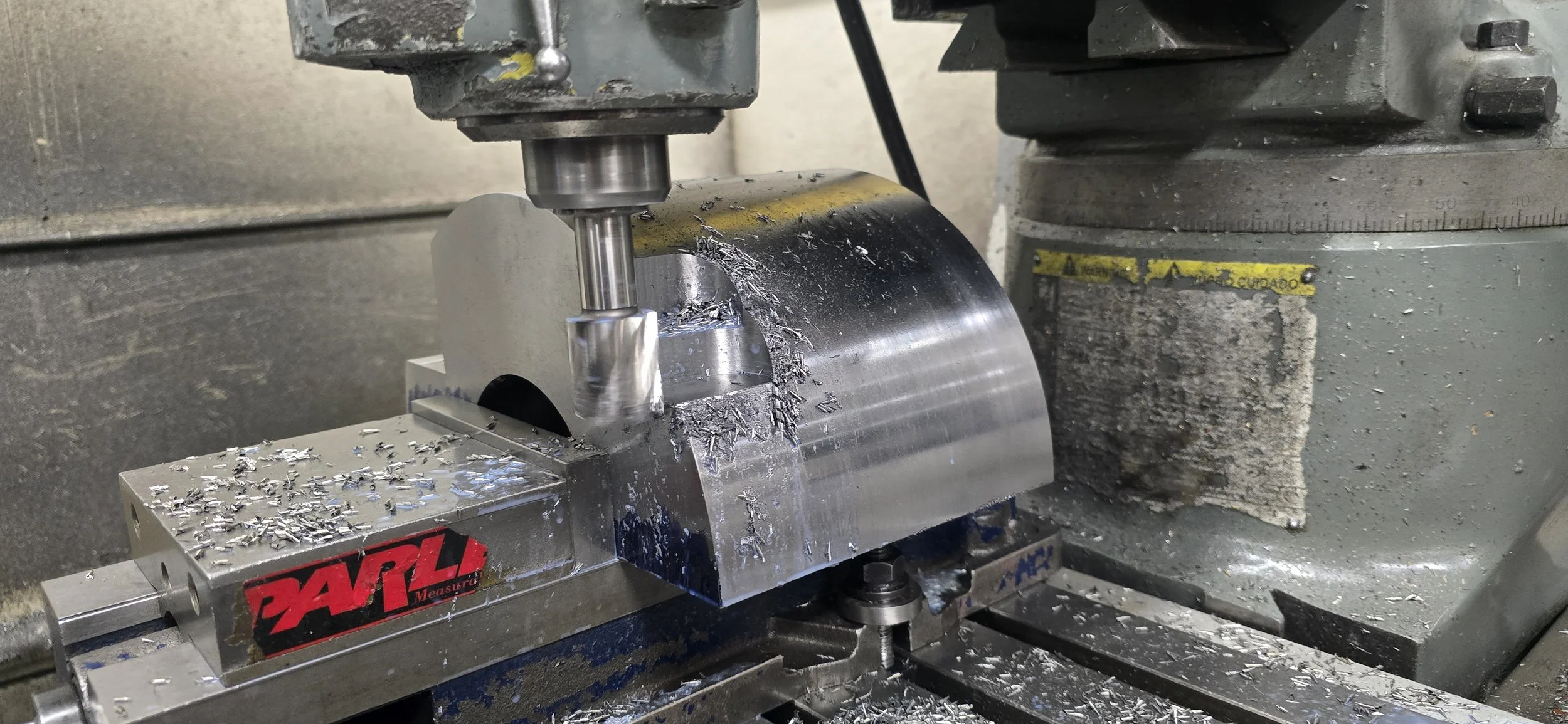 A metal lathe machine shaping a cylindrical metal piece, with metal shavings scattered around.