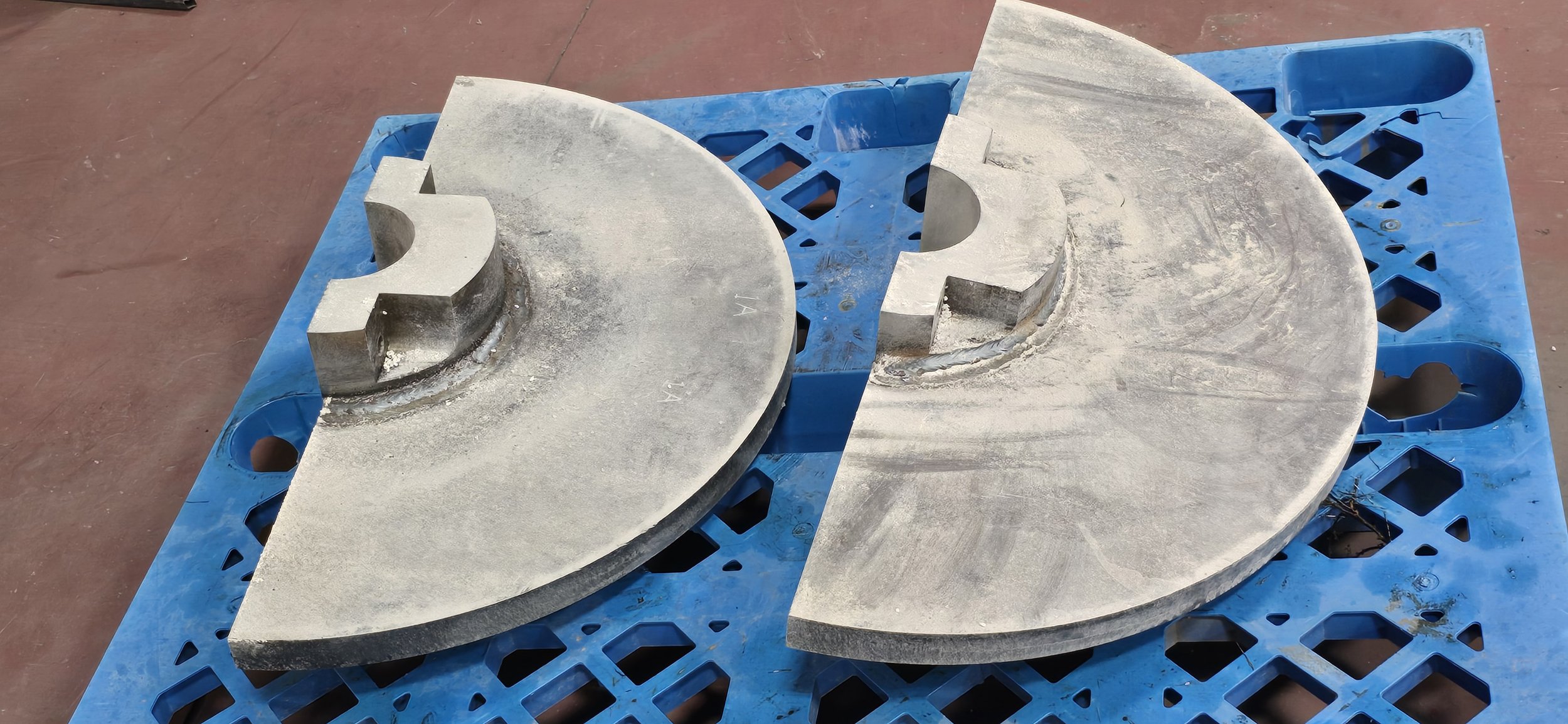 Two half-circle concrete blocks with large question marks cut out on top, resting on a blue plastic pallet.