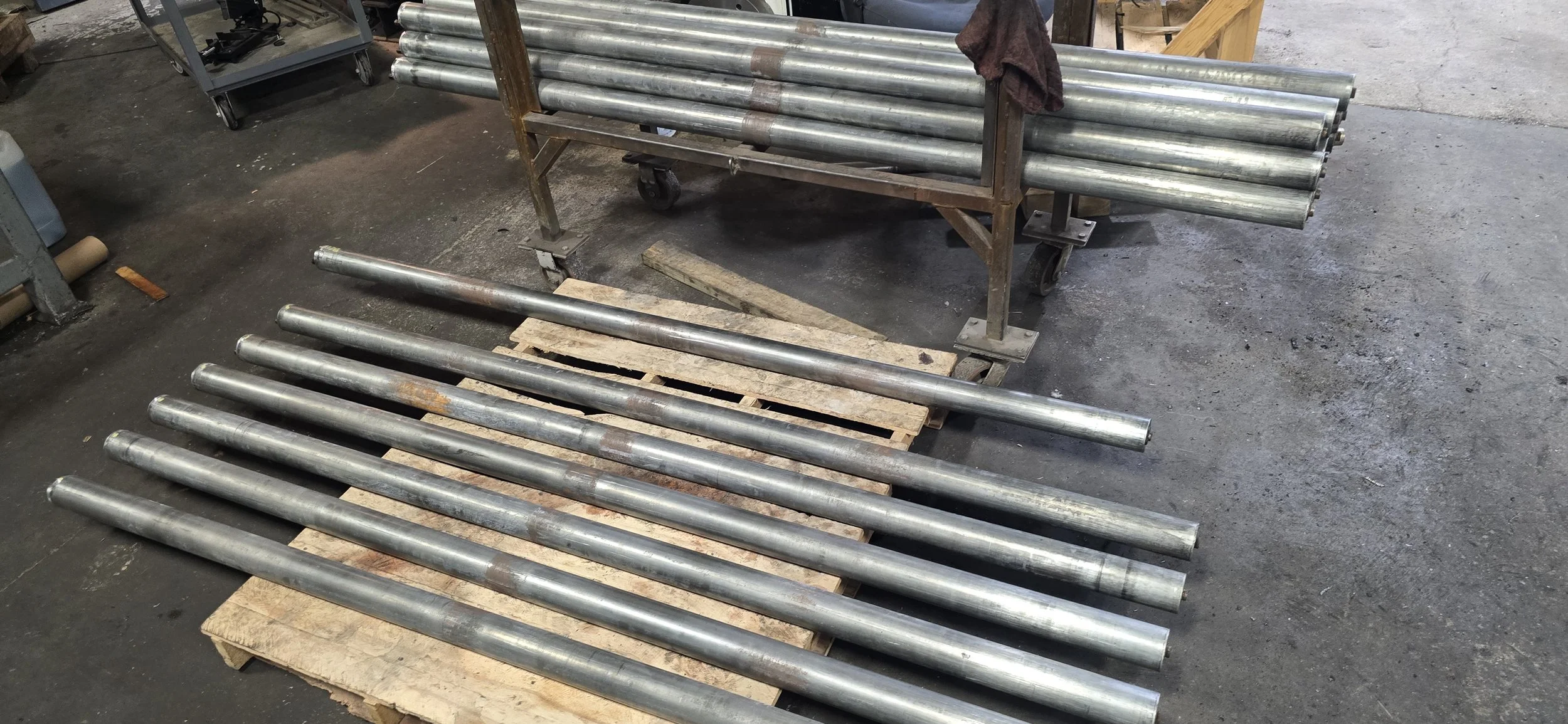 Multiple metal pipes are arranged on a pallet and a cart in an industrial workshop.