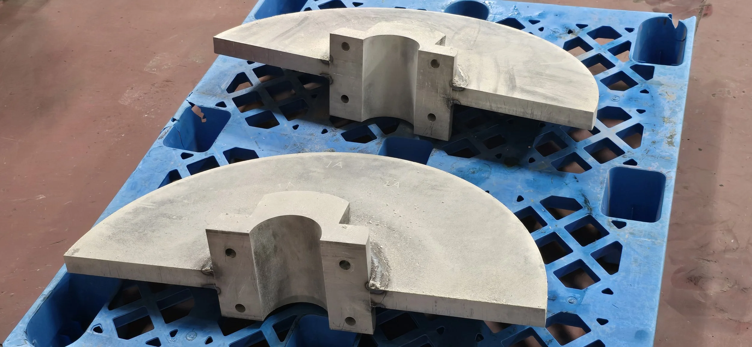 Two large semi-circular metal components with attached rectangular blocks on top, placed on a blue plastic pallet.