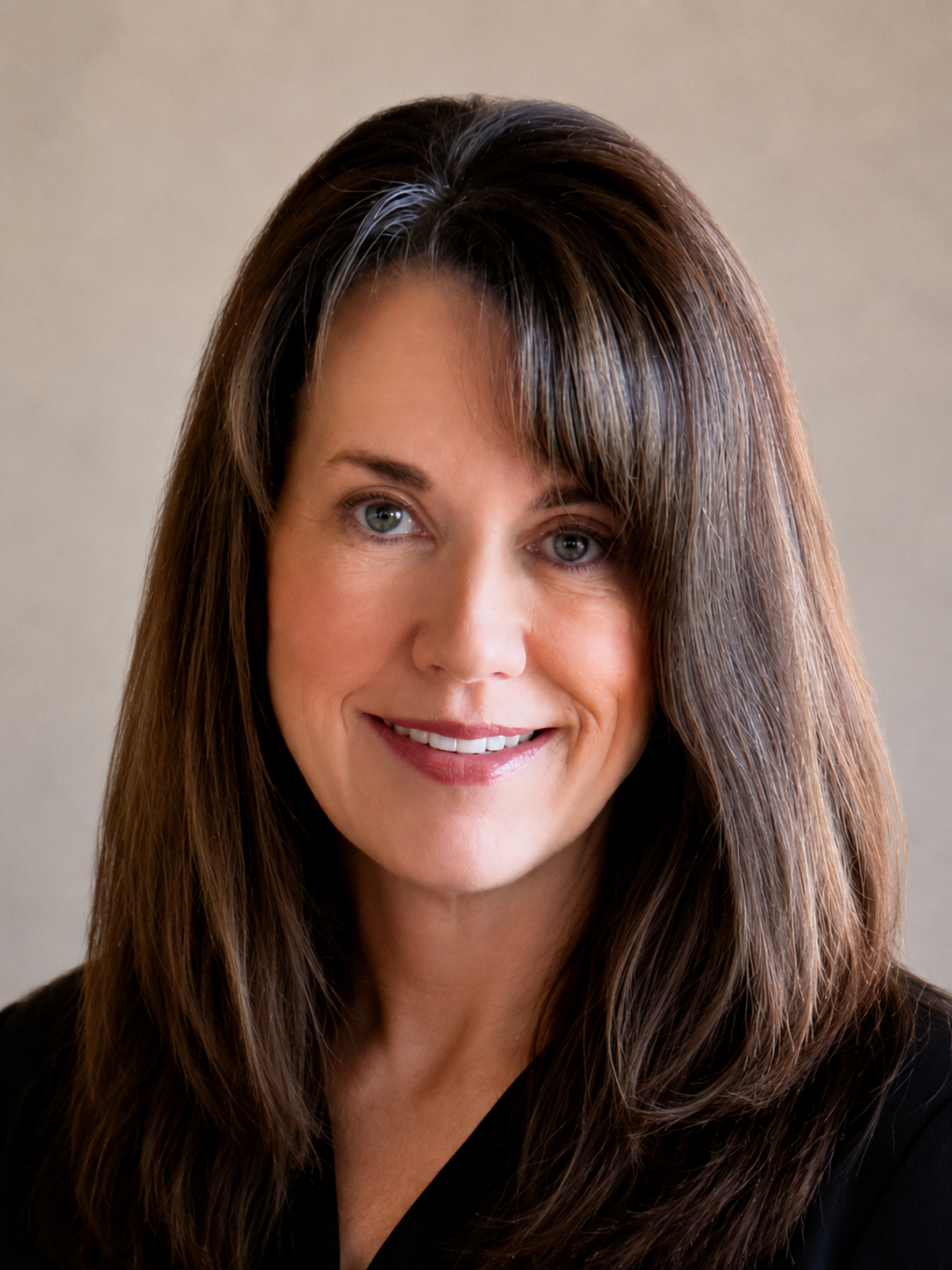 Close-up of a smiling woman with long brown hair and blue eyes, wearing a black top.