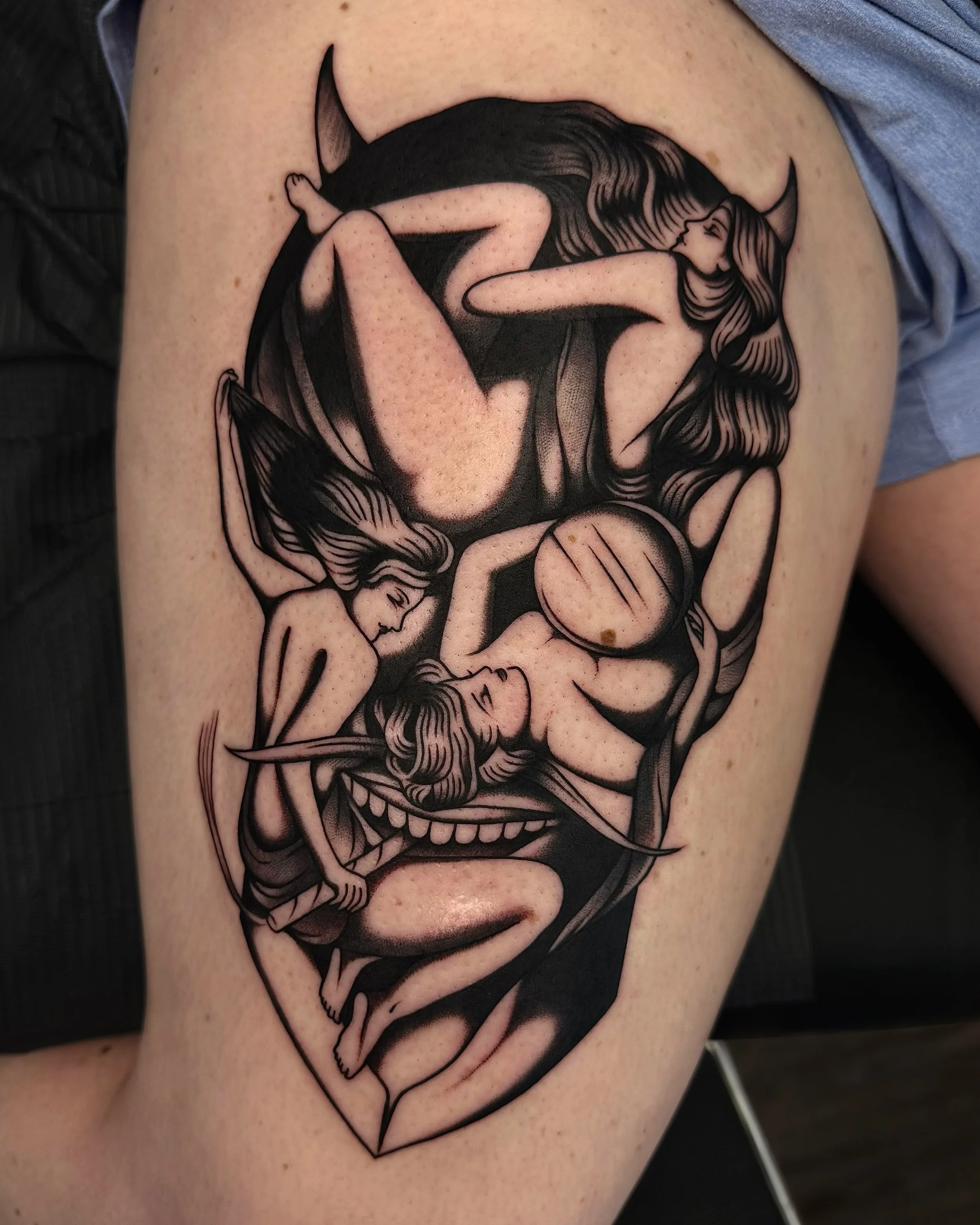 Black and gray tattoo of three nude women with pointed ears, intertwined with a demon-like creature with large teeth and horns, and a moon, all within a diamond-shaped border.
