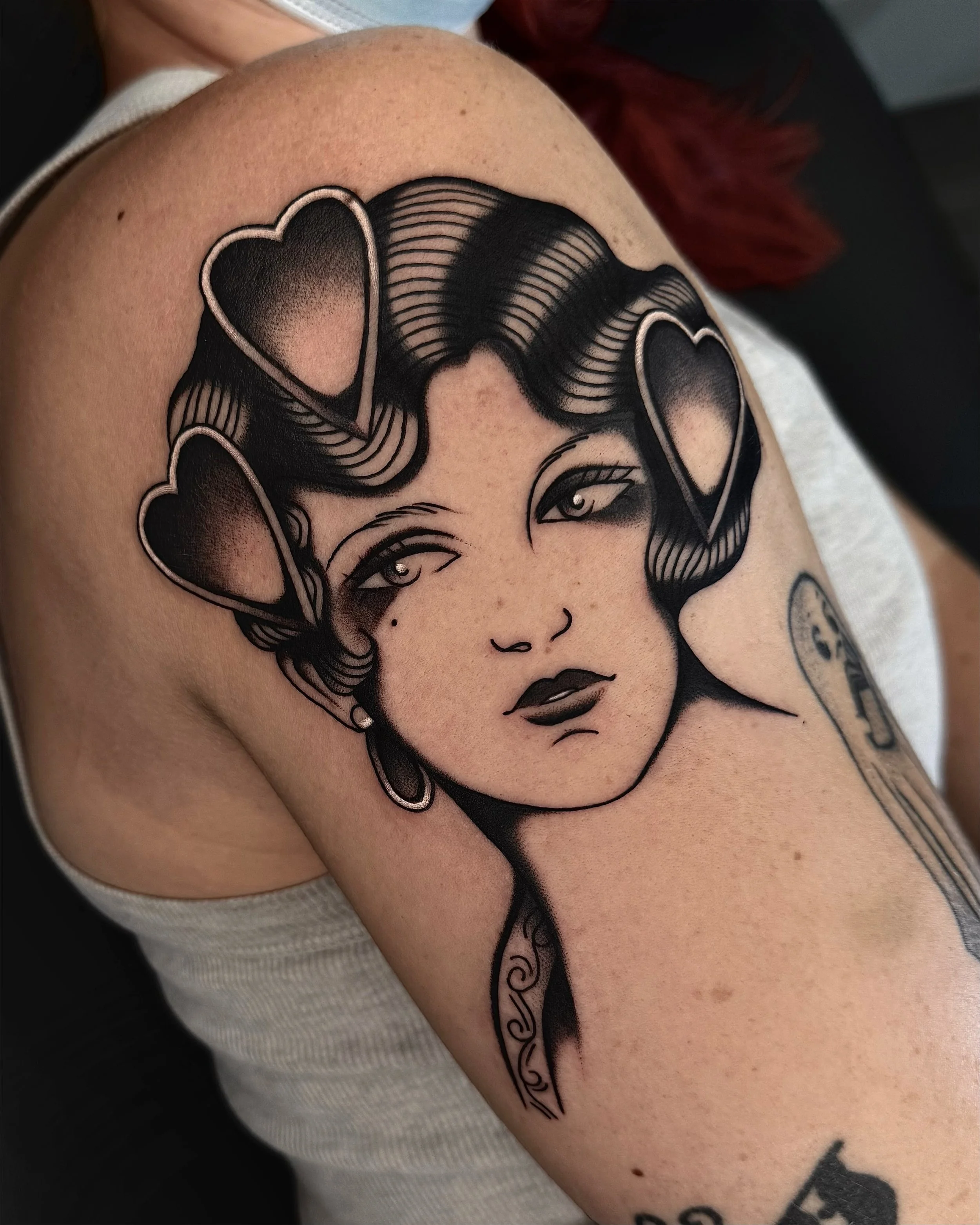 Tattoo of a woman's face with wavy hair, hearts in her hair, and a vintage microphone on her shoulder.