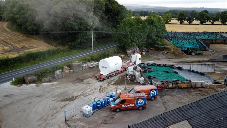 Aerial view of a farm yard with the wrapped silo on its trailer beside the silage clamp, a McCaskie van parked alongside and fields beyond