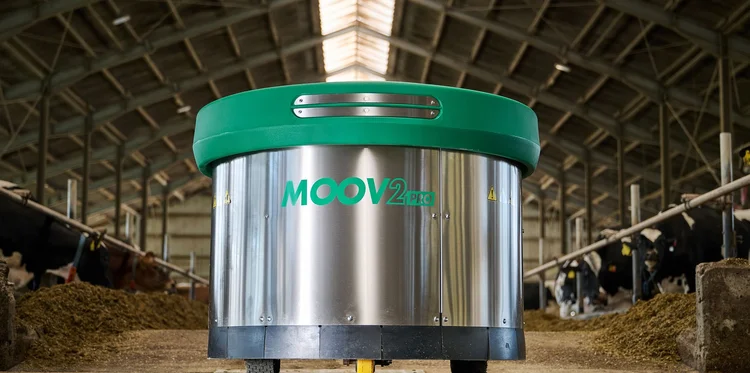 A JOZ Moov 2PRO feed pusher coming head-on down a feed passage, cows eating at the barrier on either side