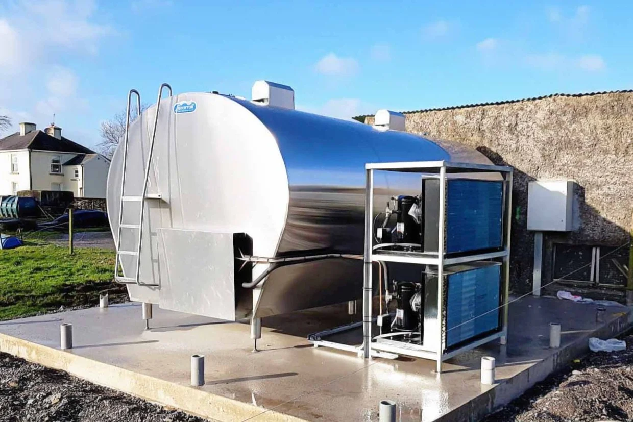 A Liscarroll stainless steel bulk milk tank installed outdoors on a concrete base, with an access ladder and an external refrigeration unit beside it