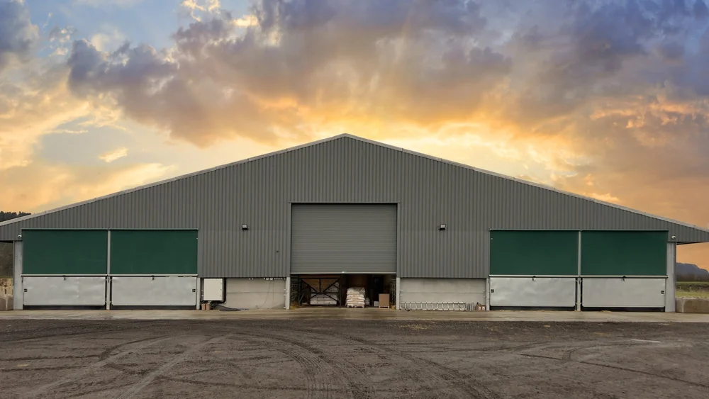 A finished Galebreaker installation at sunset: green roller screens fitted either side of the roller door on a grey farm shed