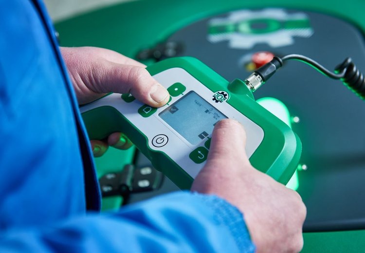 A farmer in a blue jacket holding the JOZ handset against the Moov 2PRO's cover, thumb on the screen
