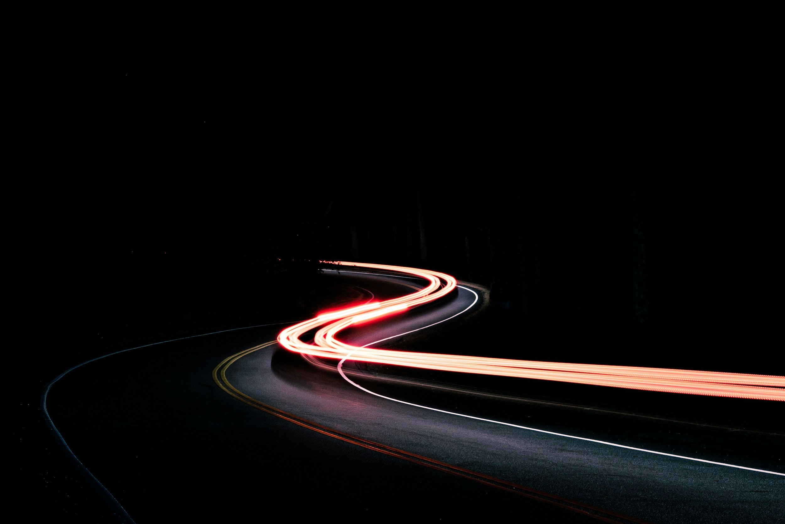 Long exposure photograph of a winding road at night with streaks of red and white car lights.