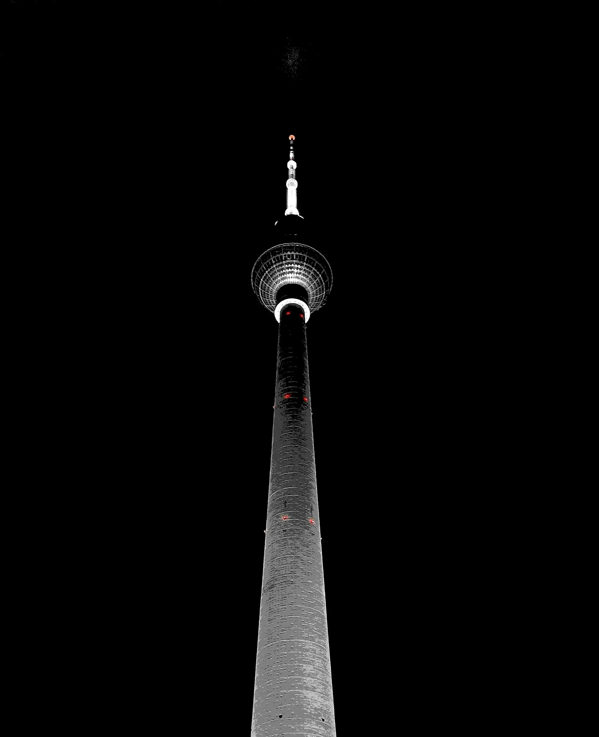 Nighttime photo of a tall communication tower with bright white lights highlighting its structure, disappearing into the dark sky.
