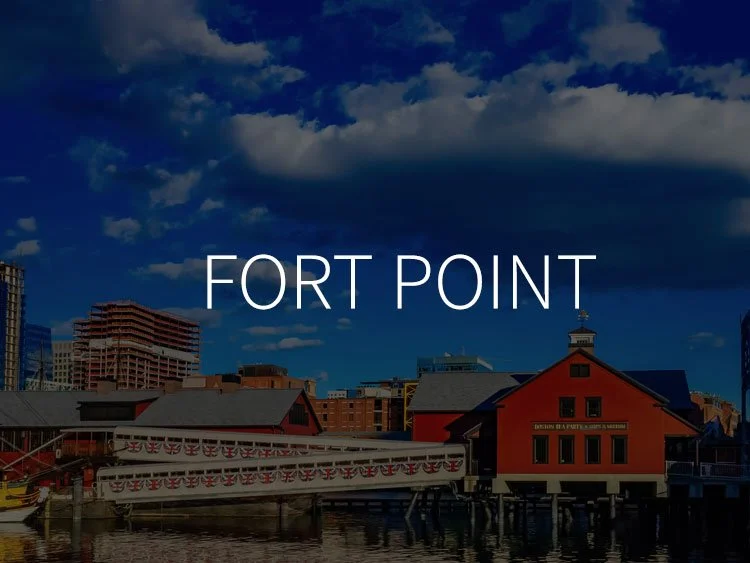 Photo of a harbor in Fort Point with historic buildings, modern city buildings in the background, under a blue sky with clouds.