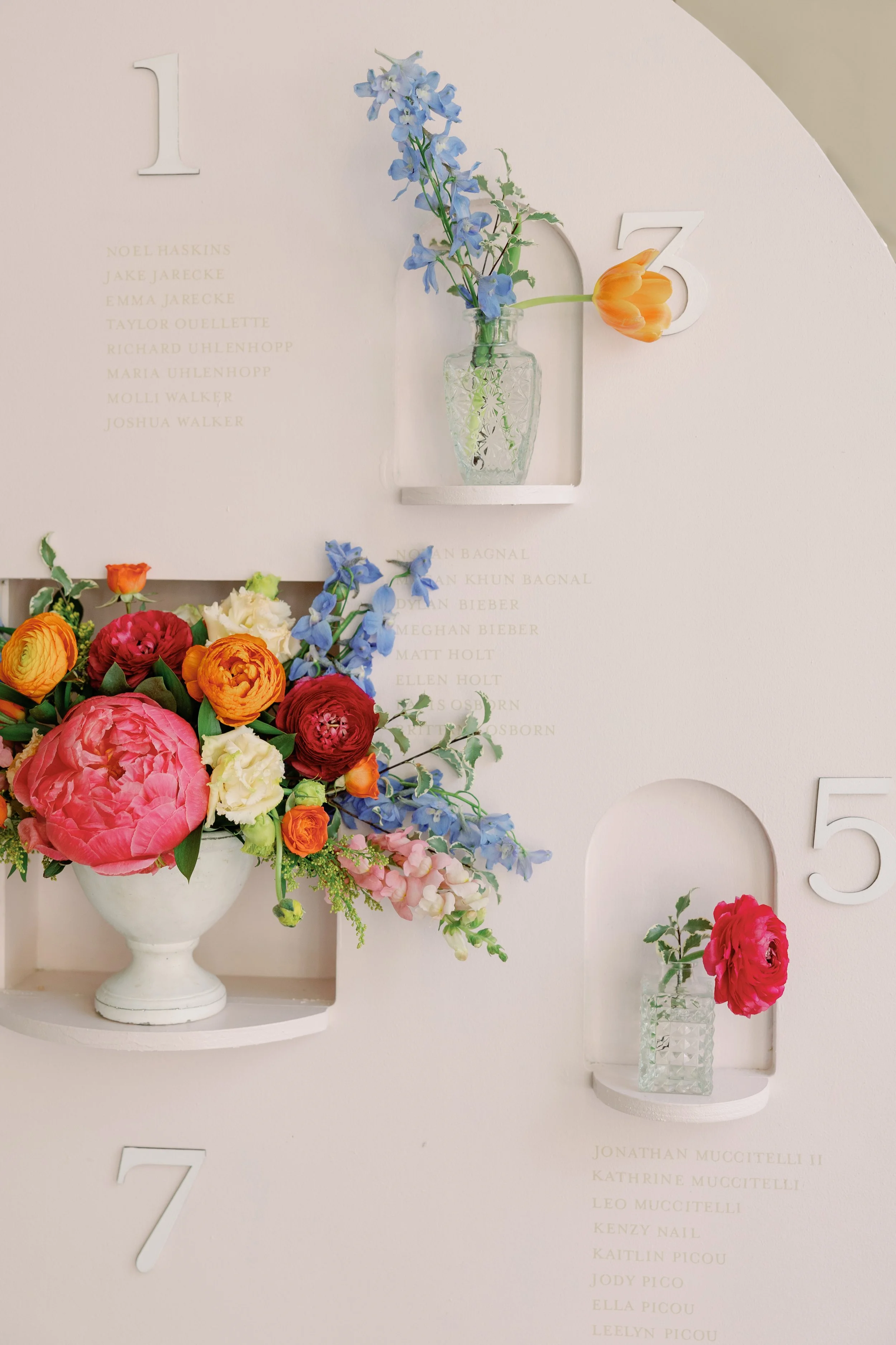 Fall Wedding at Cannon Green in Charleston SC designed by Bouquets and Bowties and captured by Wild Cotton Photography. Colorful floral arrangement with pink, red, orange, and yellow flowers in a white vase on a seating chart display.