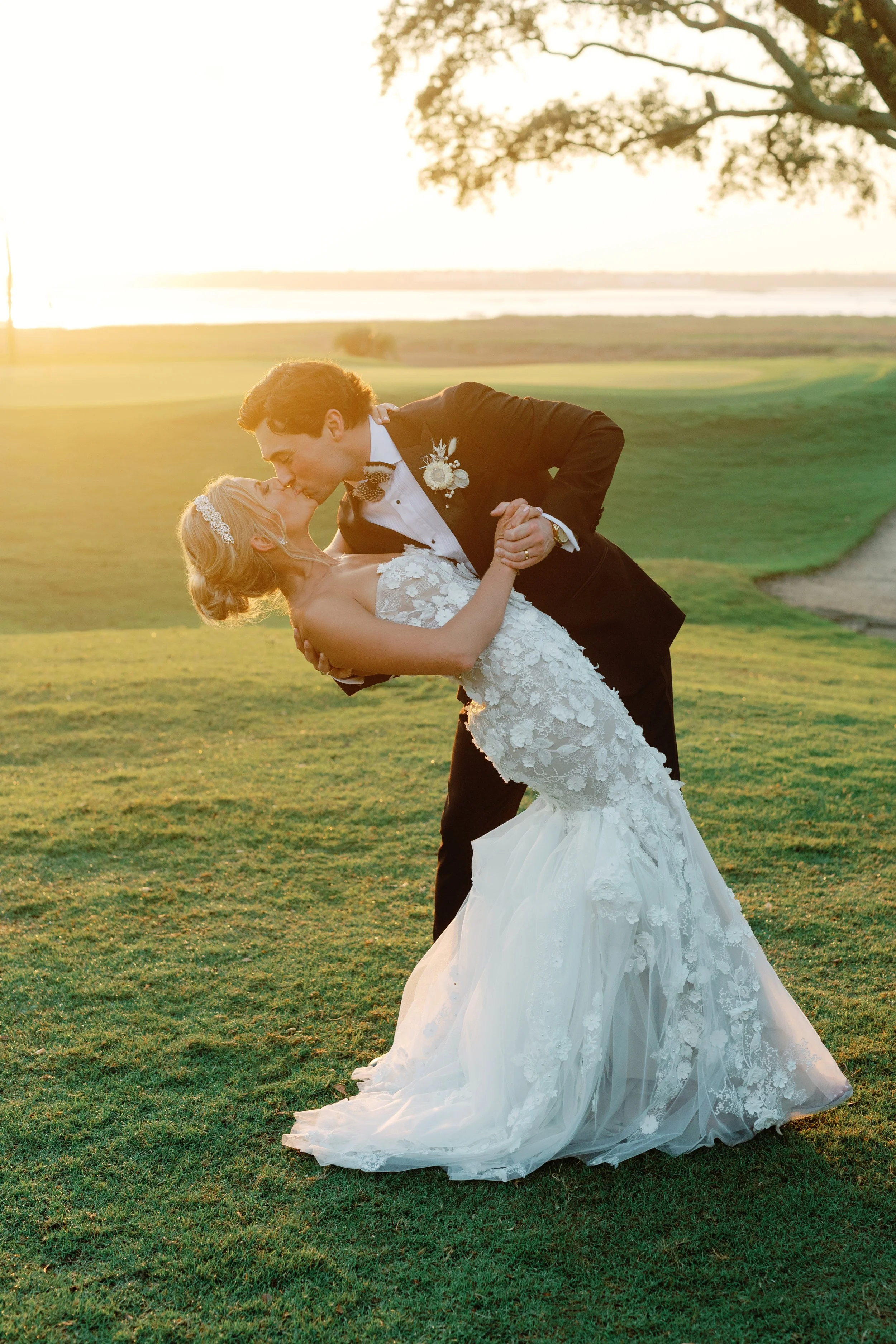 A newlywed couple sharing a kiss on a golf course at sunset, with the groom dipping the bride in a romantic pose.