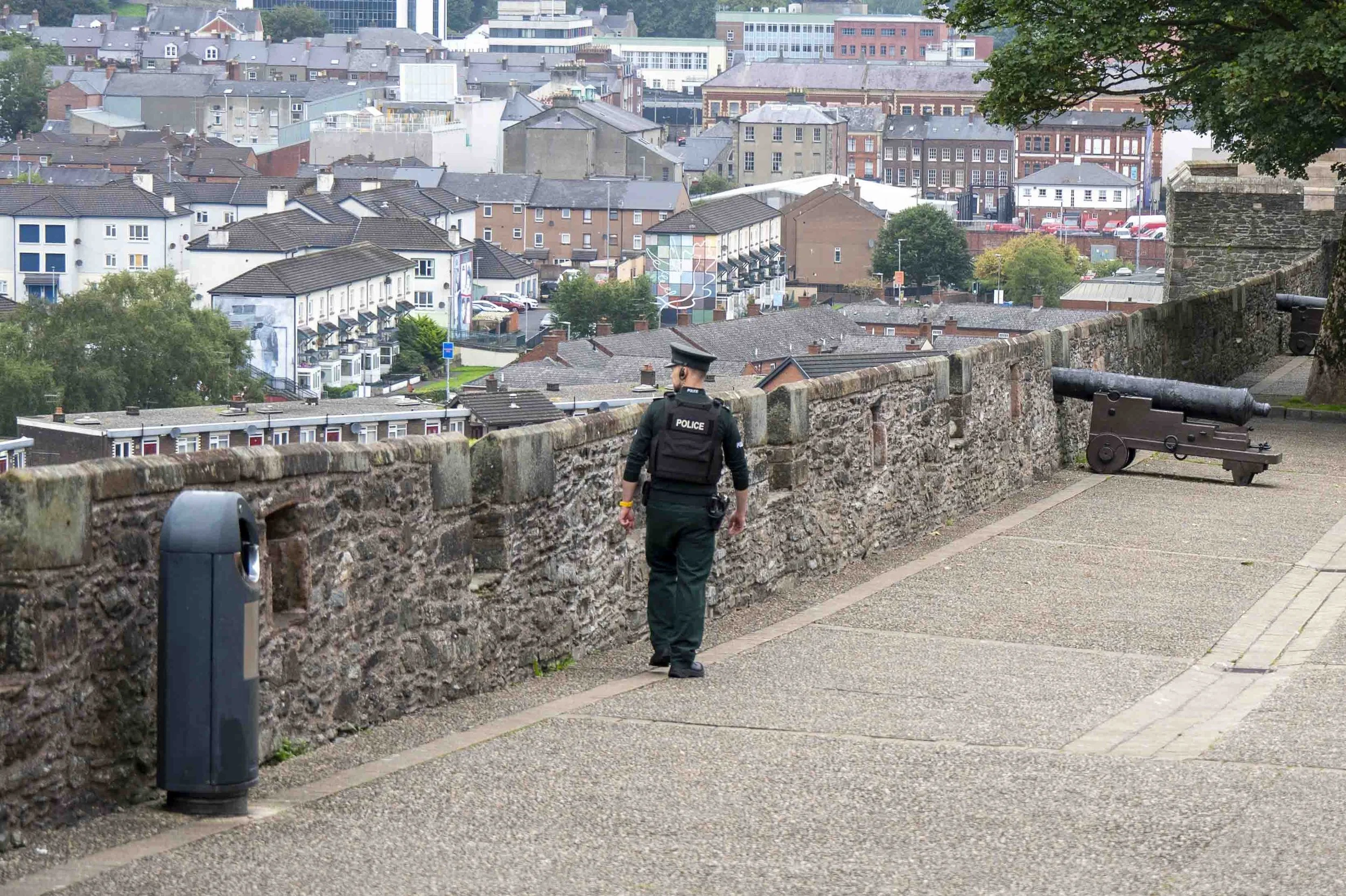 Police officer patroling the wall with the bogside peace mural in the distance