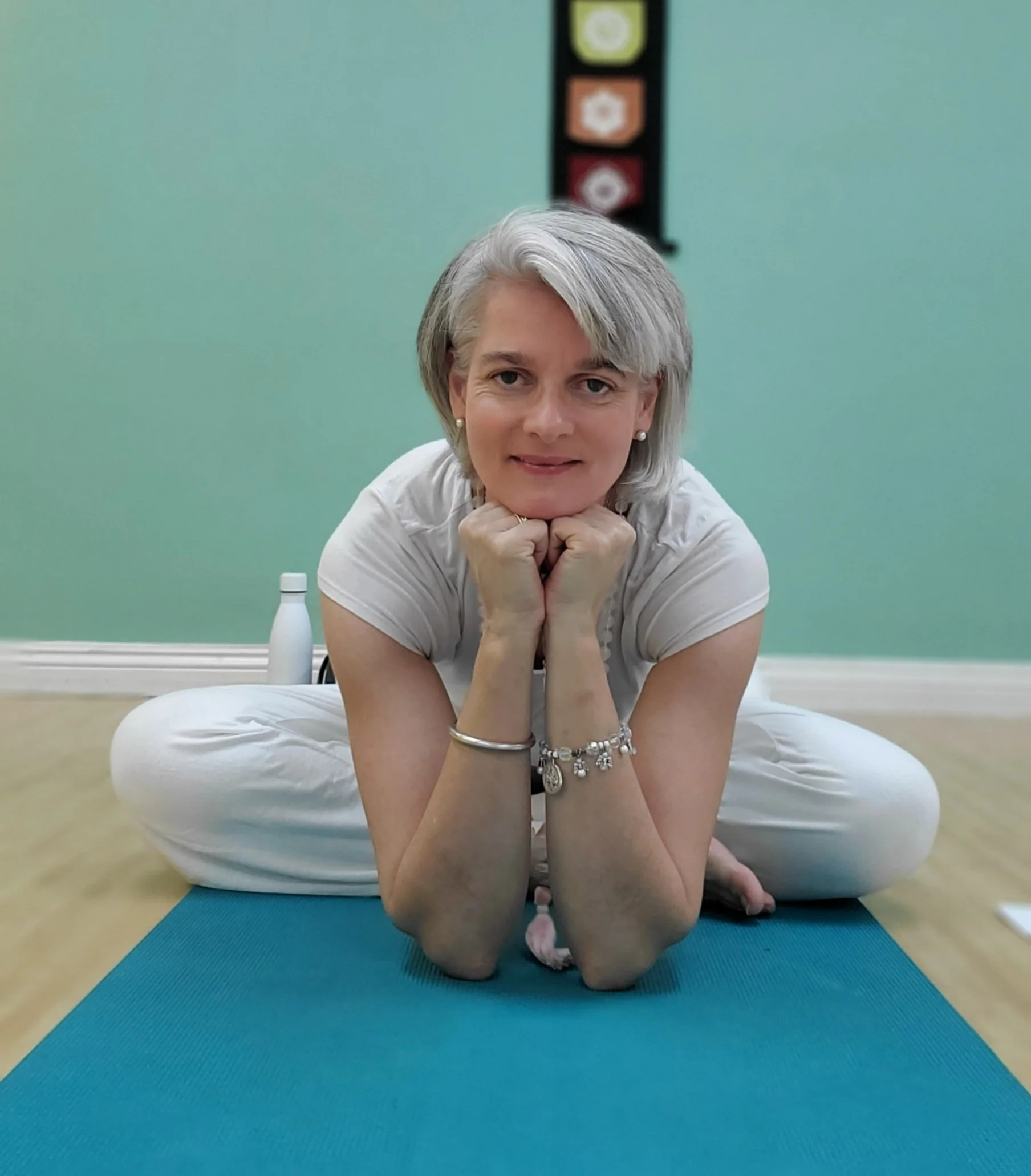 A woman with gray hair practicing yoga on a blue mat in a room with green walls.