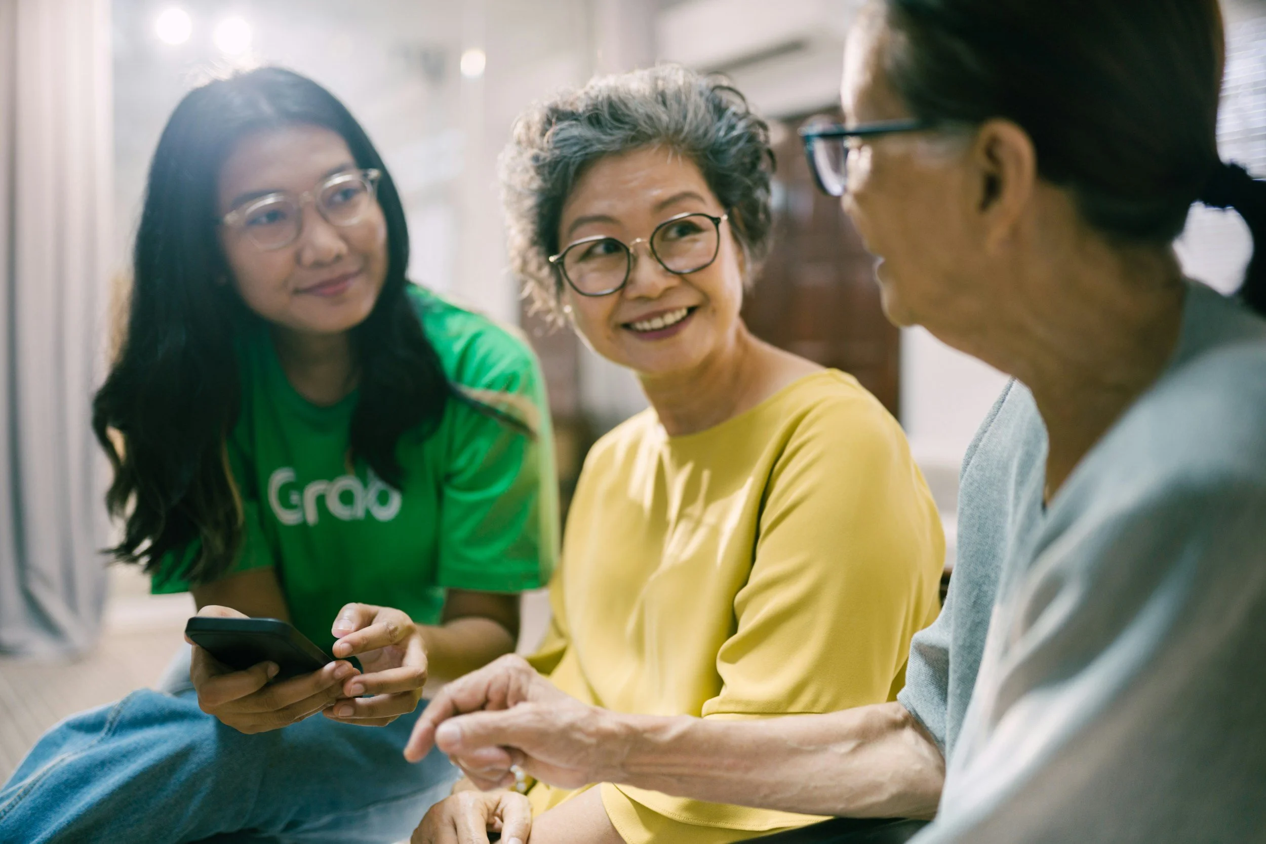 Adult daughter and granddaughter sitting beside their older mother and grandmother, sharing a supportive conversation at home.