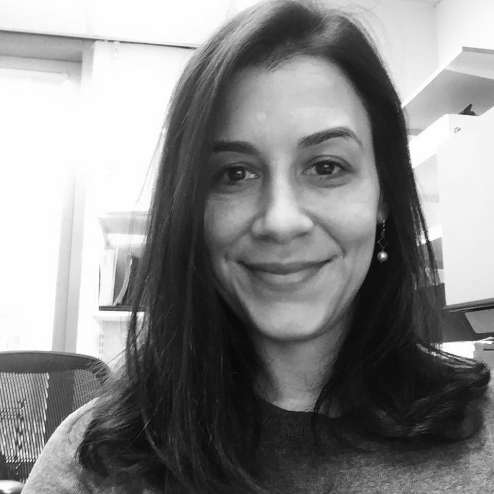 Black and white image of a smiling woman with dark straight hair, wearing a dark blouse against the backdrop of an office