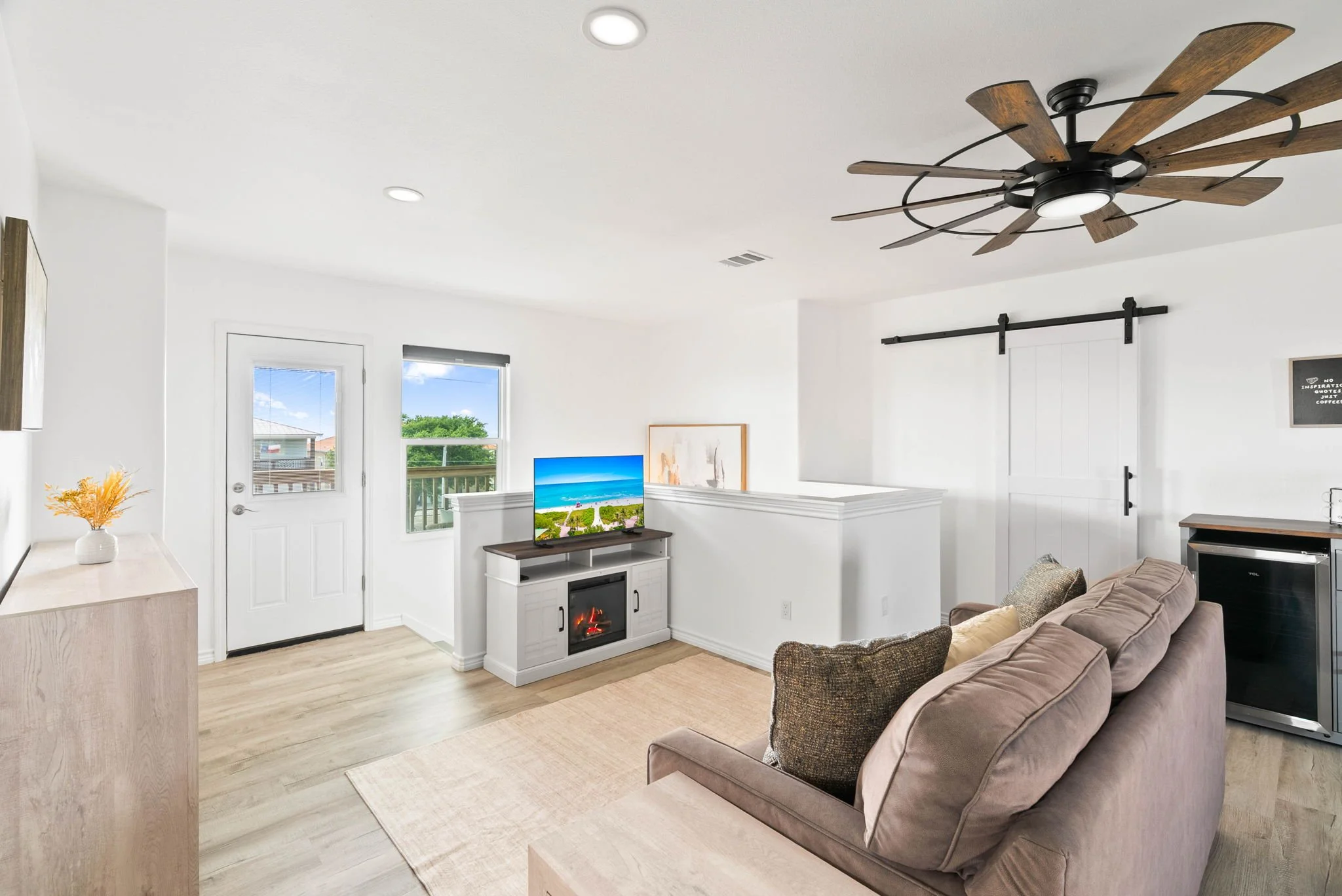 Upper-level lounge with sofa, electric fireplace, TV, beverage fridge and balcony access