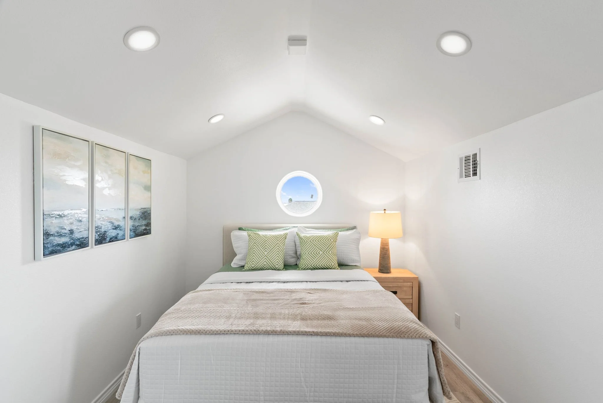 Bright loft bedroom with queen bed, coastal artwork and round porthole window