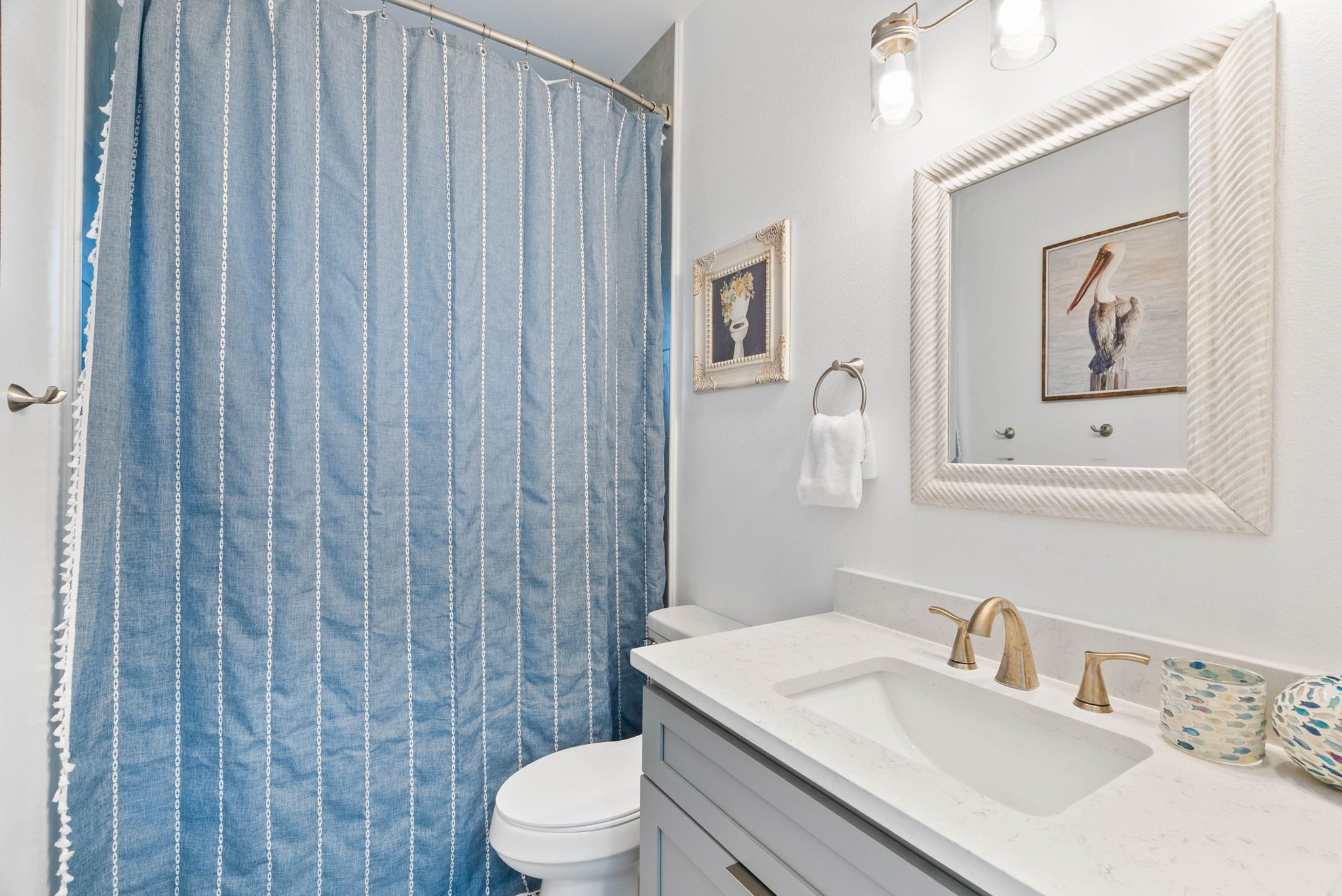 Coastal bathroom with blue shower curtain, quartz vanity and pelican artwork