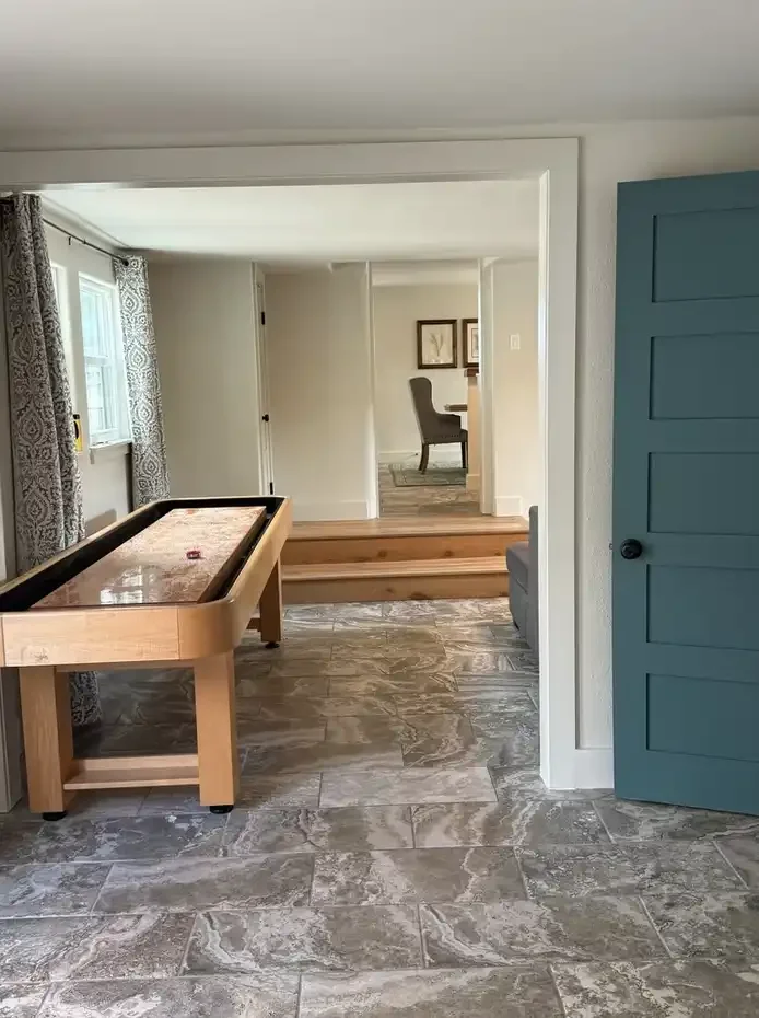 Bright game room at Skiff House featuring a shuffleboard table, tiled floors, and an open layout leading into a comfortable sitting area.