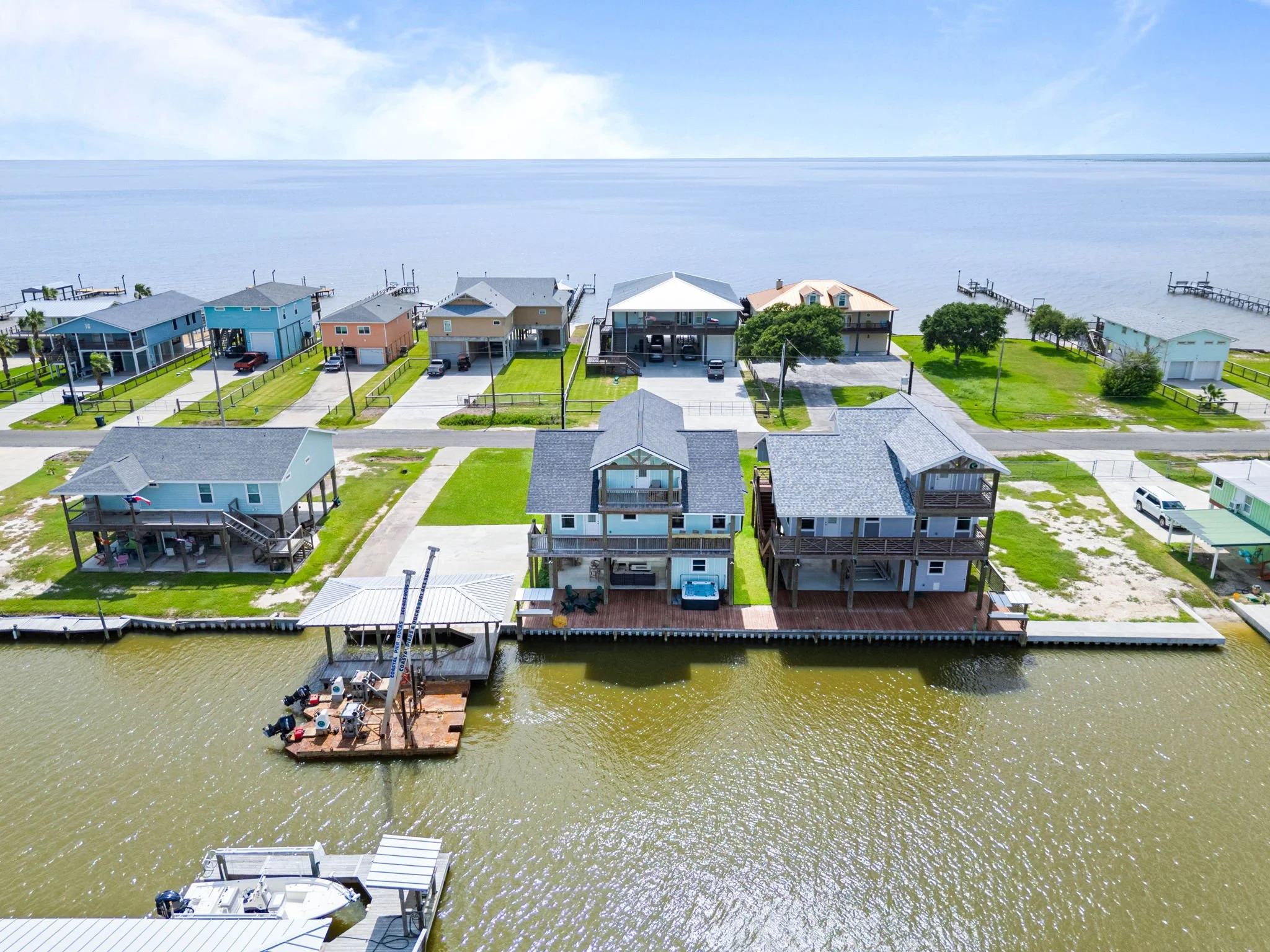Canal-side aerial of the coastal home with waterfront deck, boat dock and bay beyond