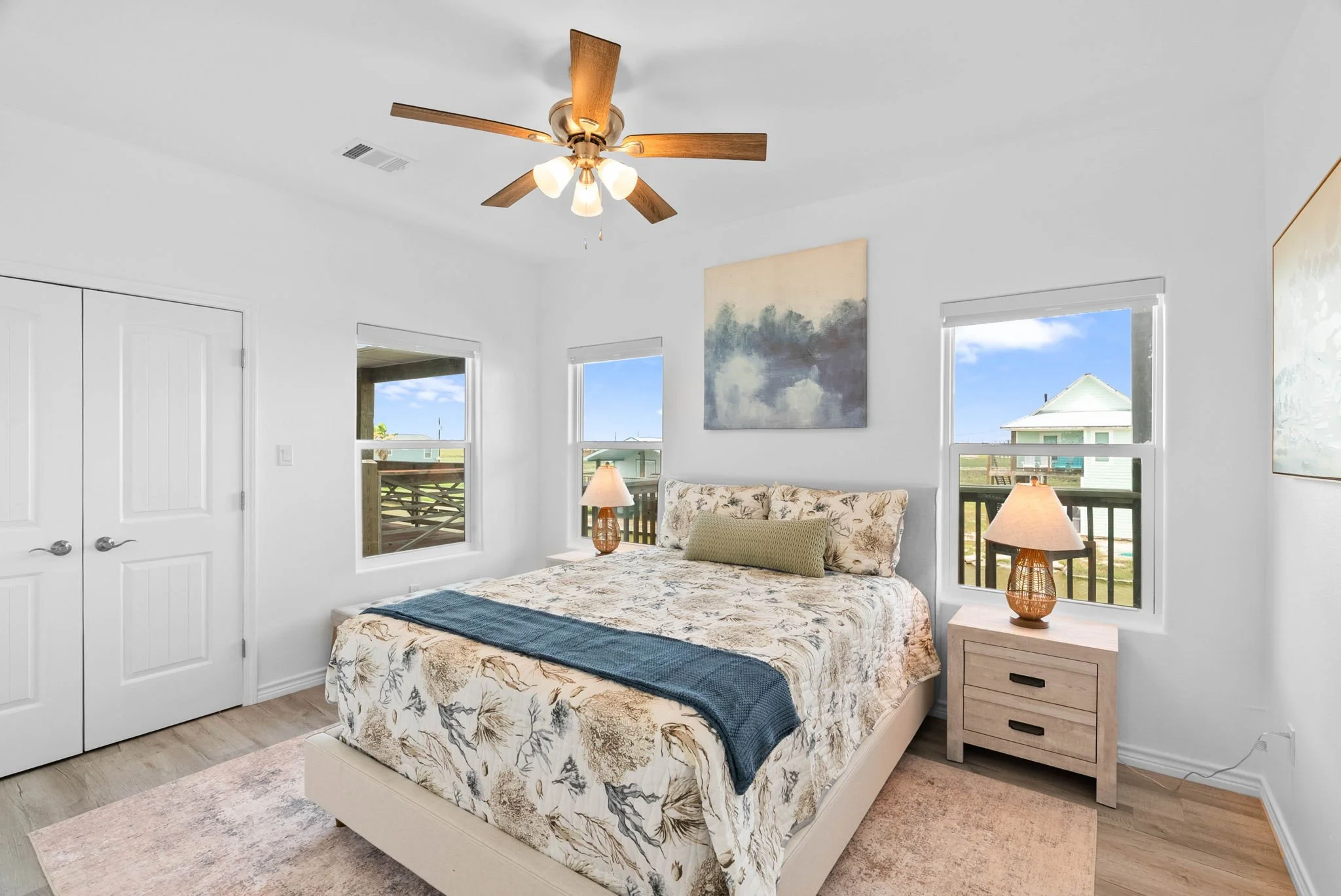 Coastal queen bedroom with floral bedding, ceiling fan and balcony views