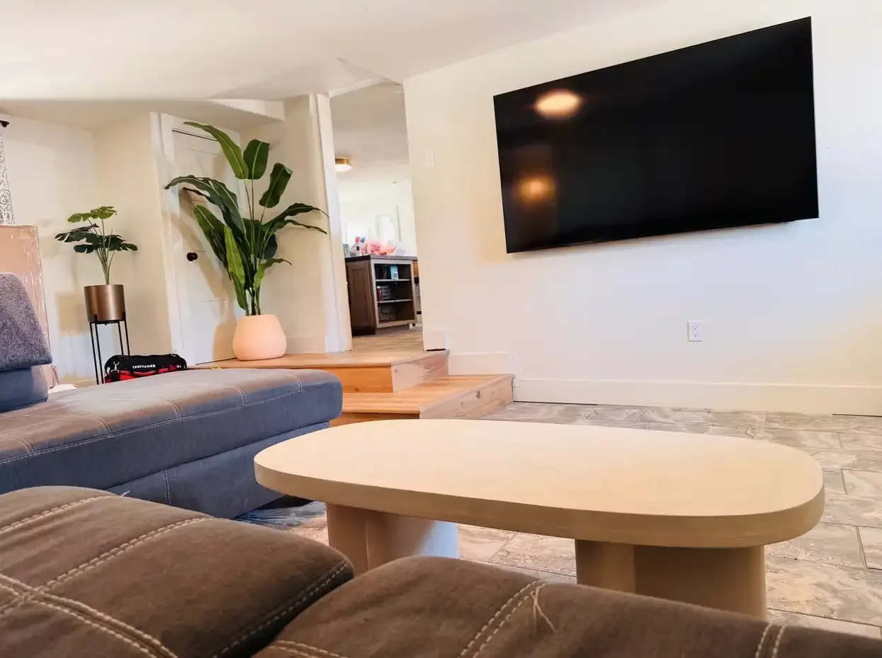 Modern living area at Skiff House with wall-mounted TV, neutral seating, and an open-concept design accented by natural light and greenery.