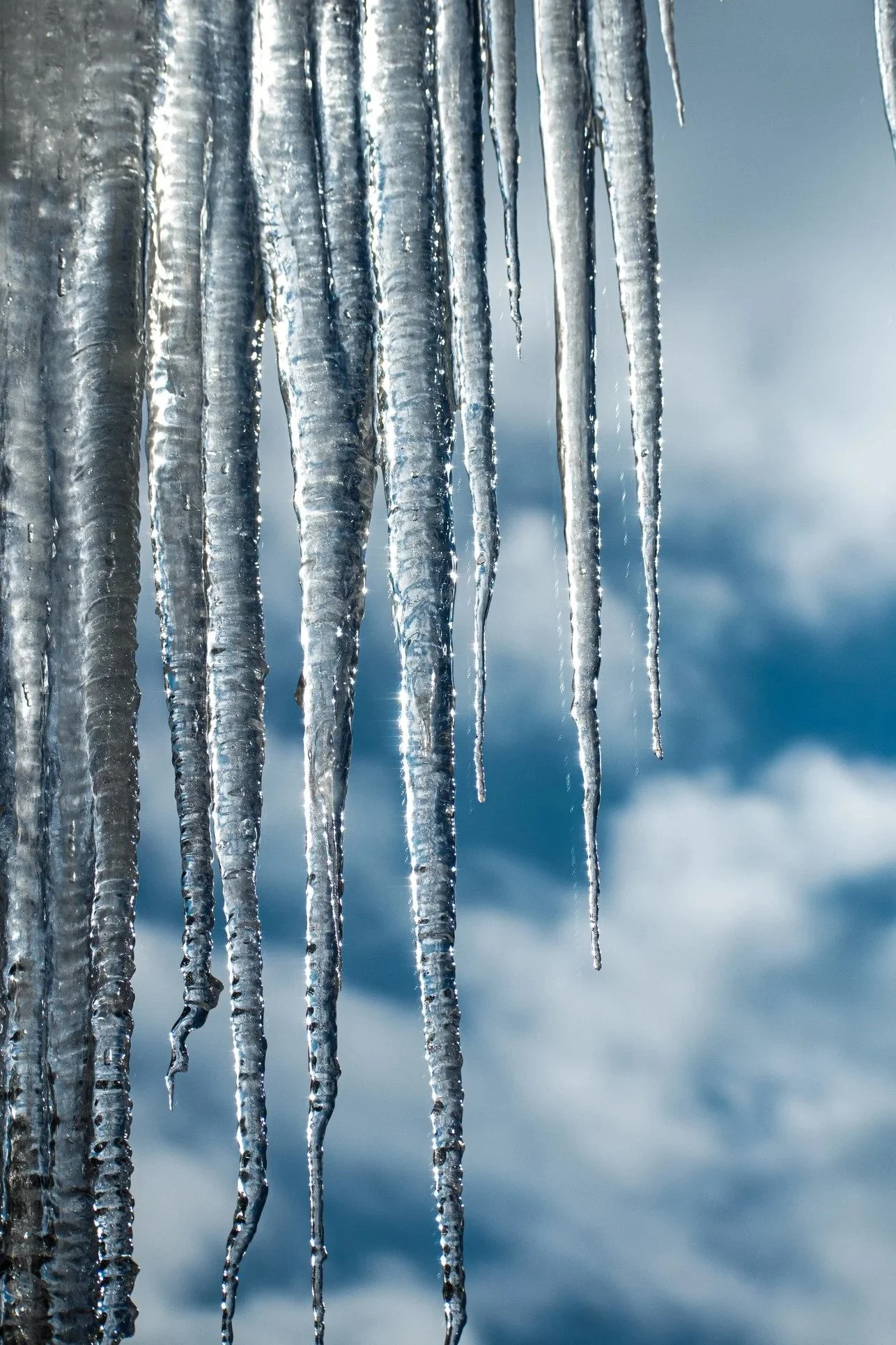 Close-up of icicles hanging against a cloudy sky background.