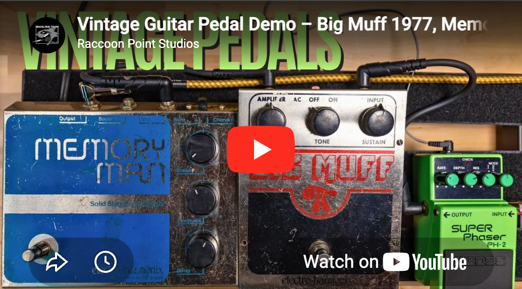 Close-up of three vintage guitar effect pedals connected with cables, including a Memory Man delay, a Big Muff distortion, and a Boss Super Phaser, set against a wooden background.