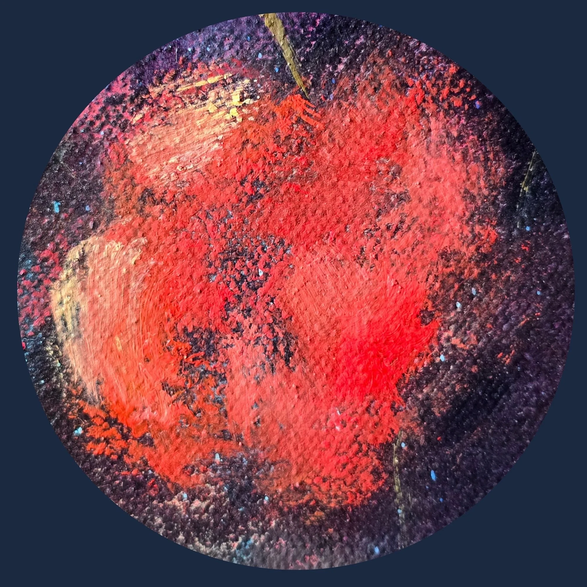 Close-up of a textured, circular object with red, black, purple, and blue speckles, resembling a painted or metallic surface.