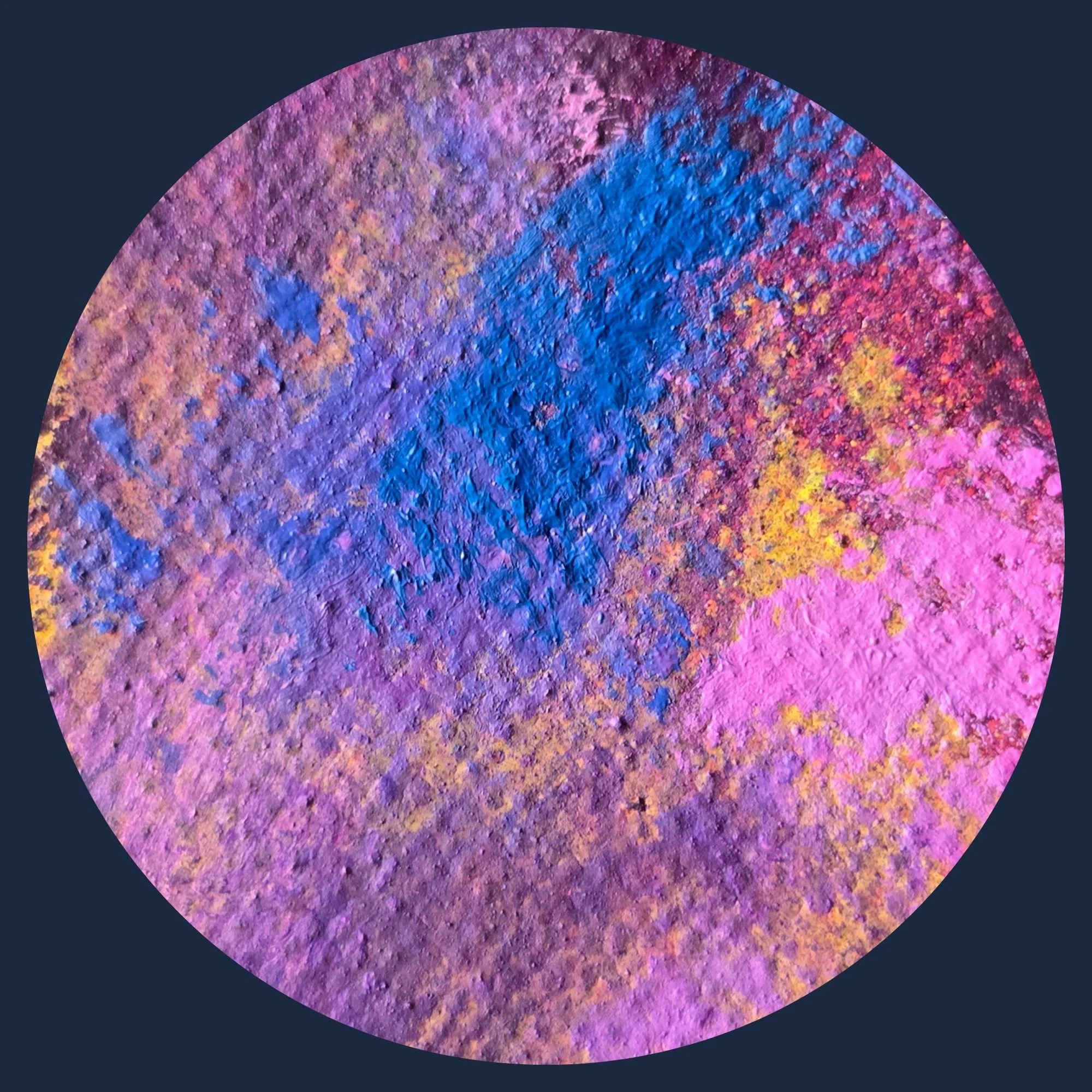 Close-up of a textured, circular surface covered in vibrant, multicolored powder in shades of purple, blue, pink, and yellow.