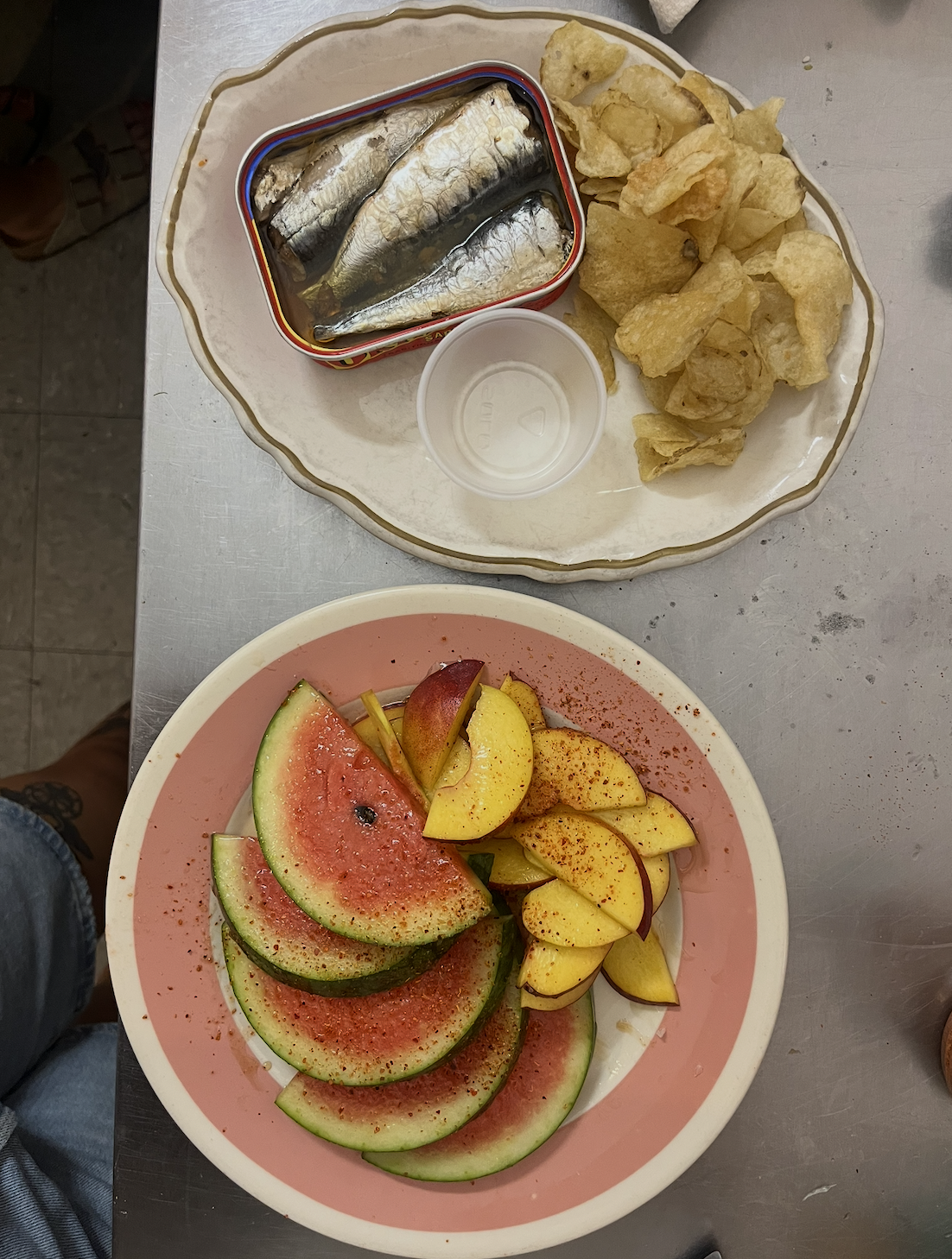 tinned fish plate with chips necxt to fresh fruit on a pink plate