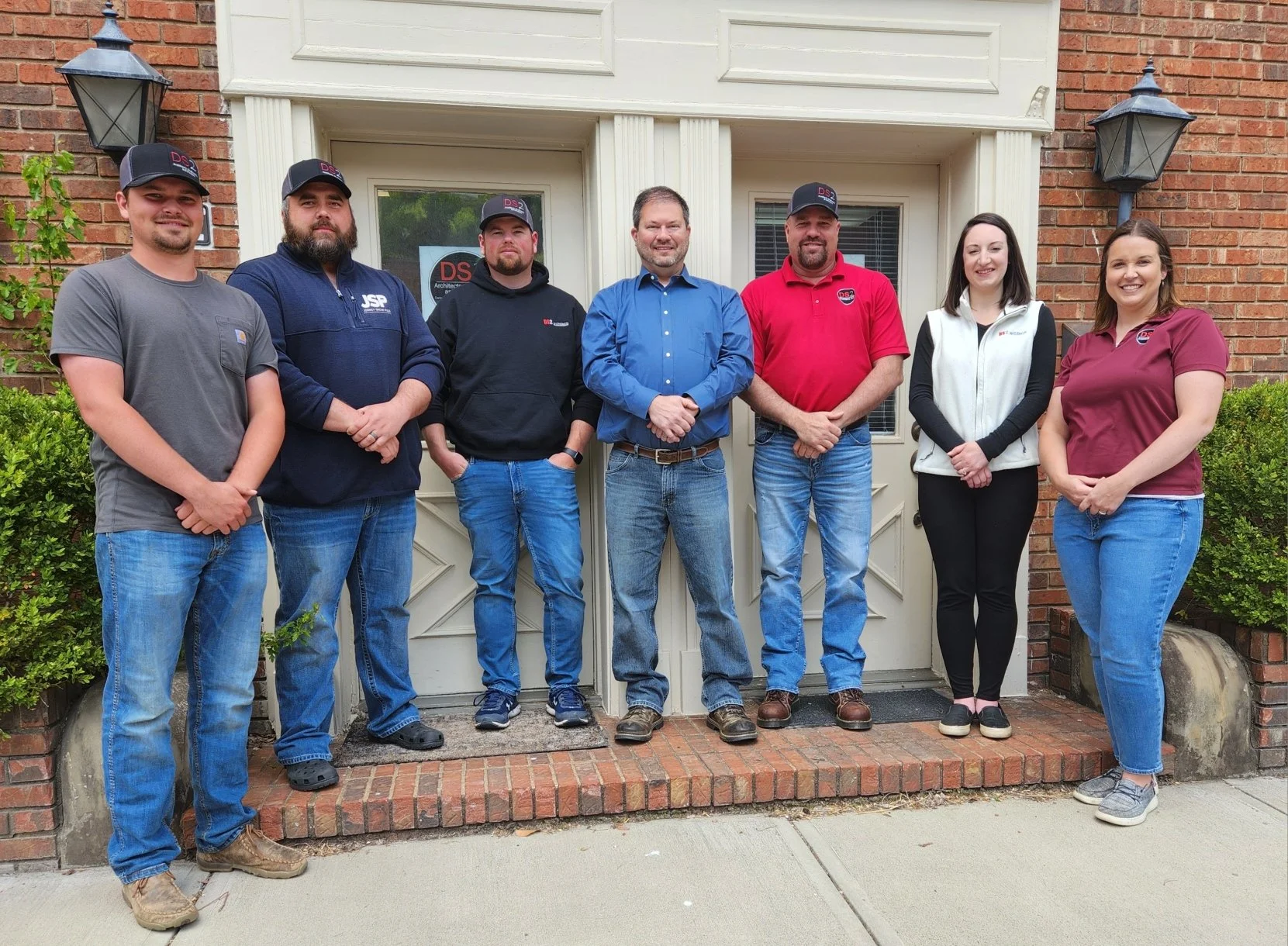 Group of seven people standing in front of a house door, smiling for the photo.