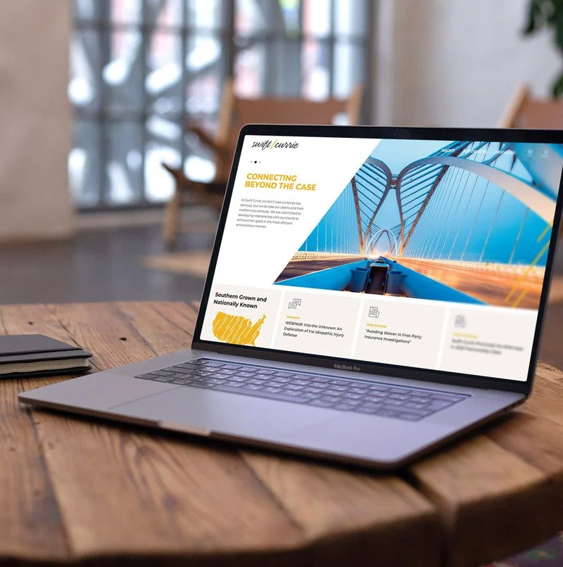 Laptop displaying Swift Currie law firm website homepage with a warm, modern layout and bridge hero image, shown on a wooden desk.