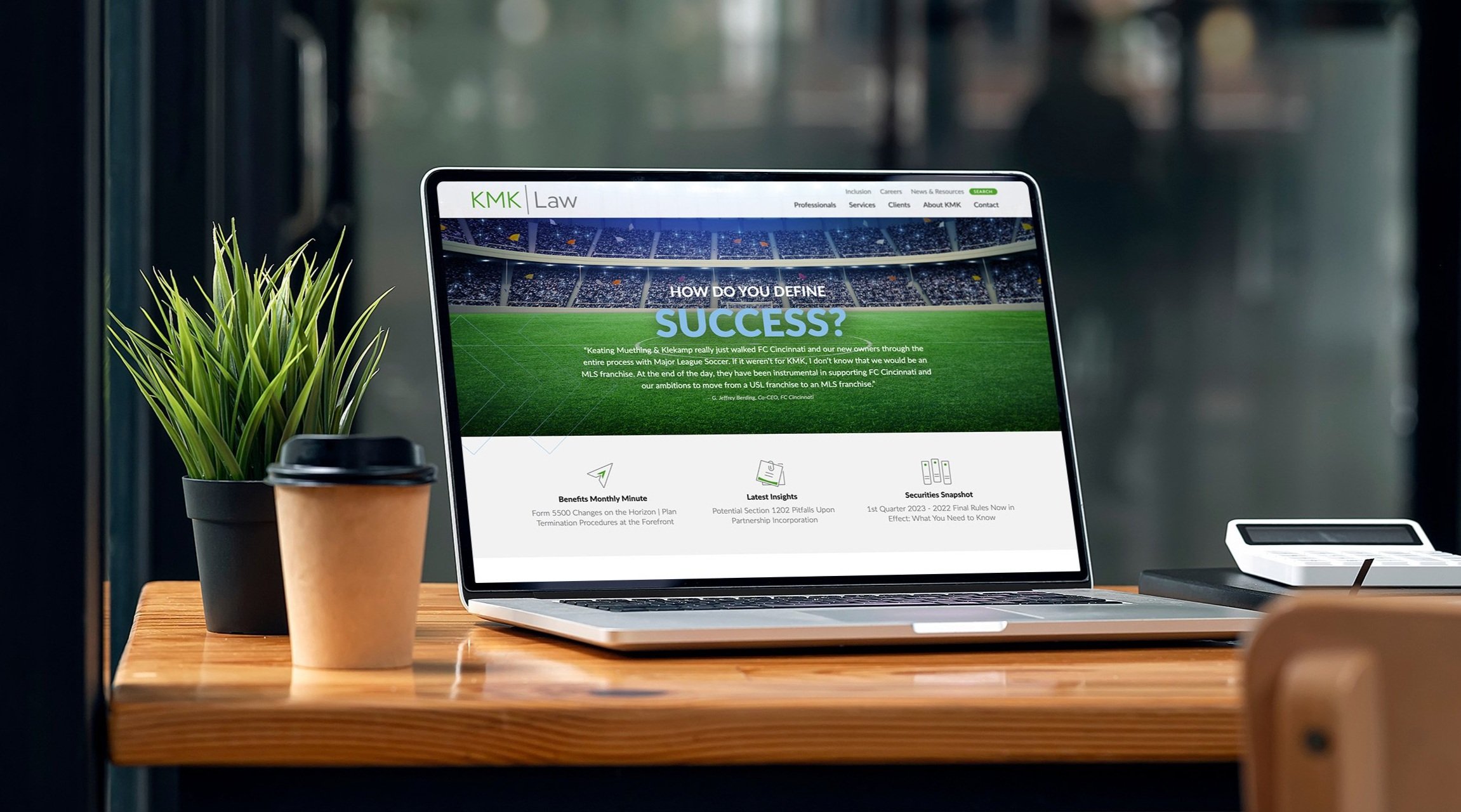 Laptop displaying KMK Law website homepage with a clean layout and green-accented hero section, shown on a desk.