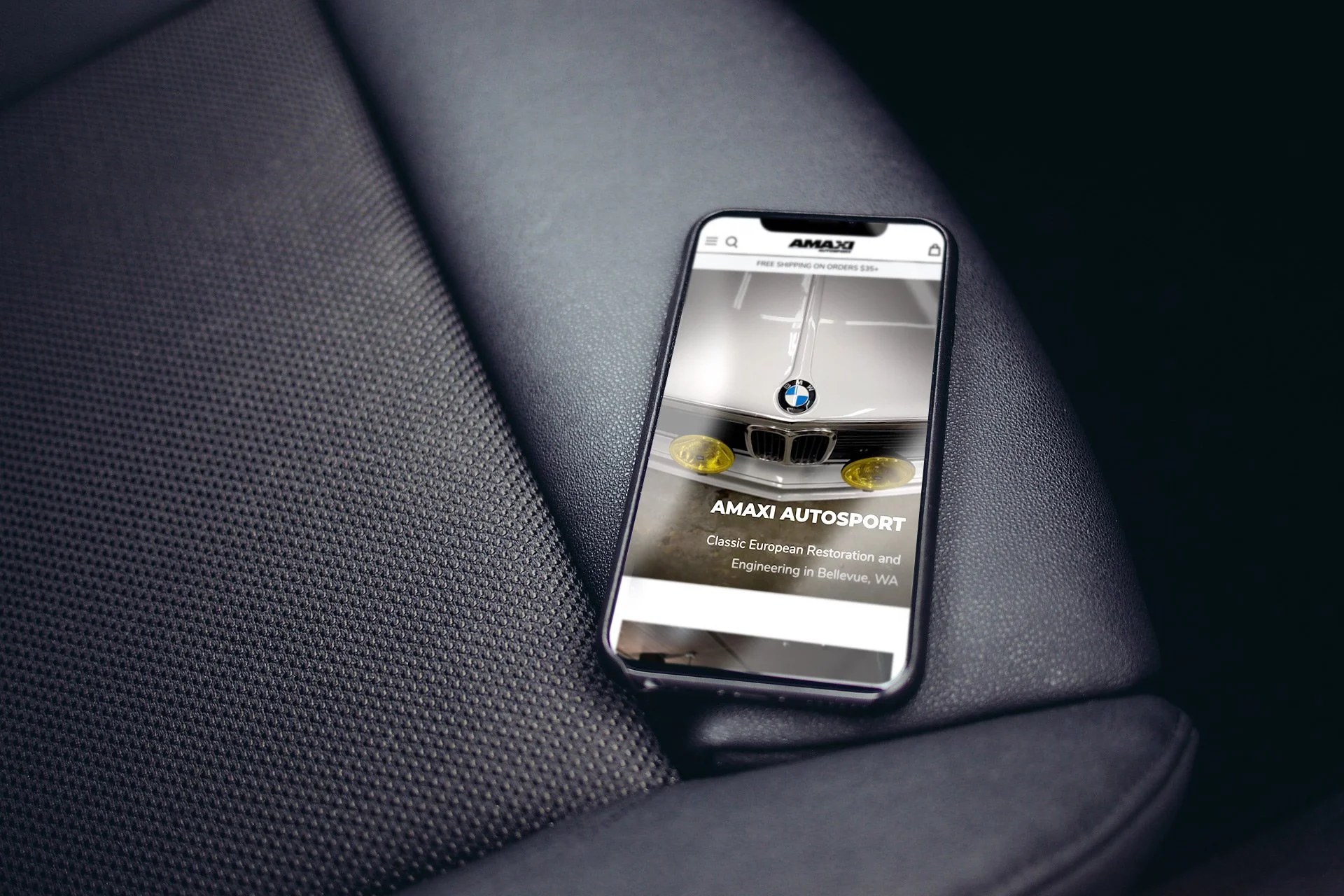 Smartphone displaying Amaxi Autosport website homepage with a clean, image-focused layout, resting on a car seat.