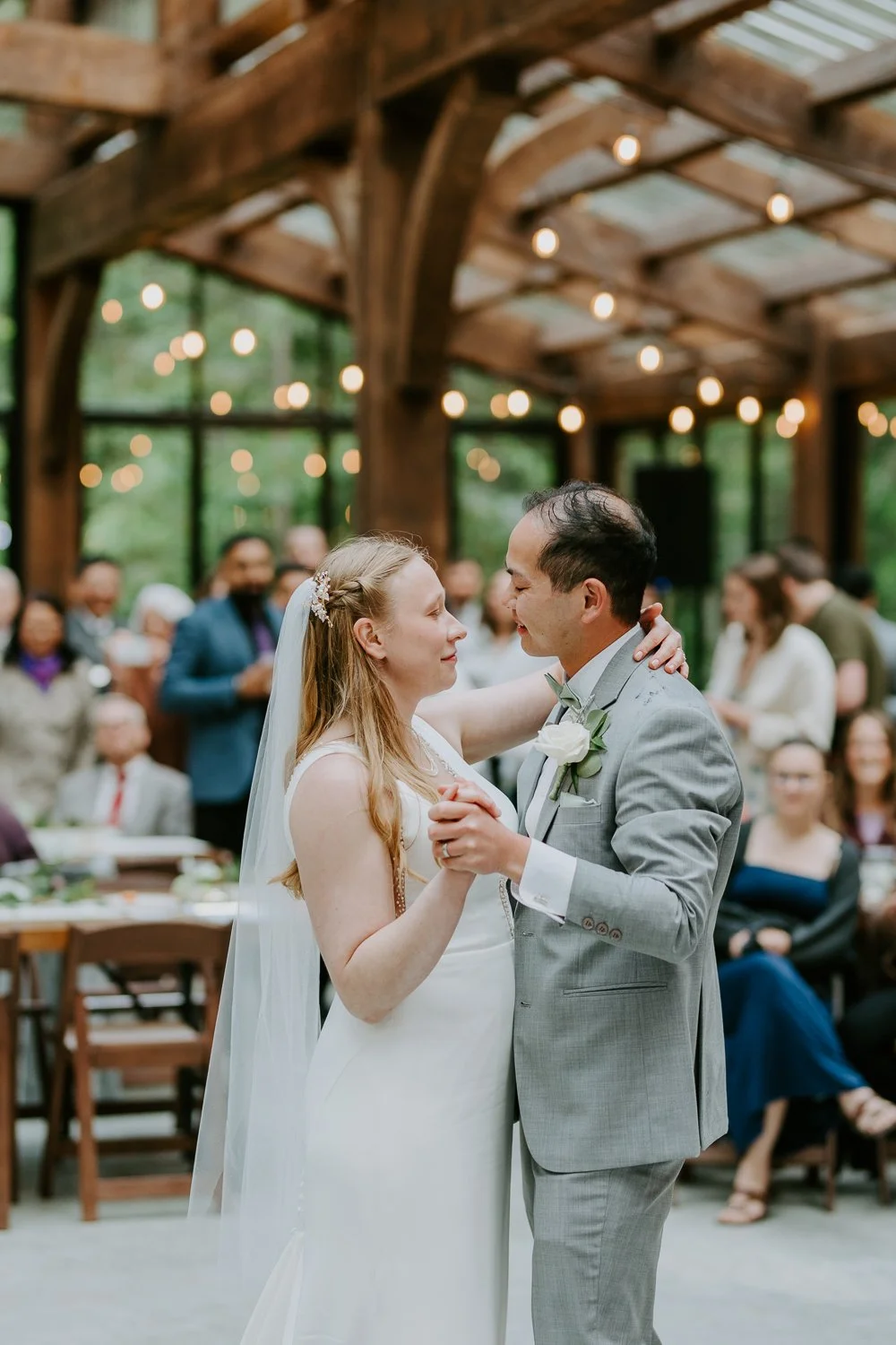 bride and groom dancing in a glass covered gazebo surrounded by twinkly lights and guests