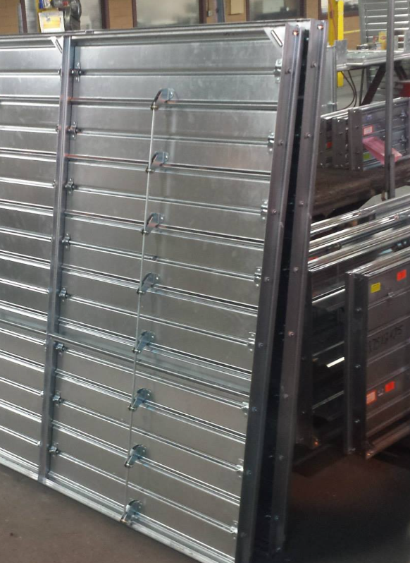 Metal panel with horizontal bars and hooks leaning against a warehouse shelving unit.
