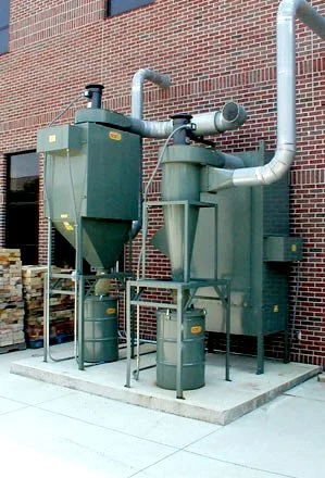 Industrial air filtration or dust collection system outside a brick building with ductwork and filters.