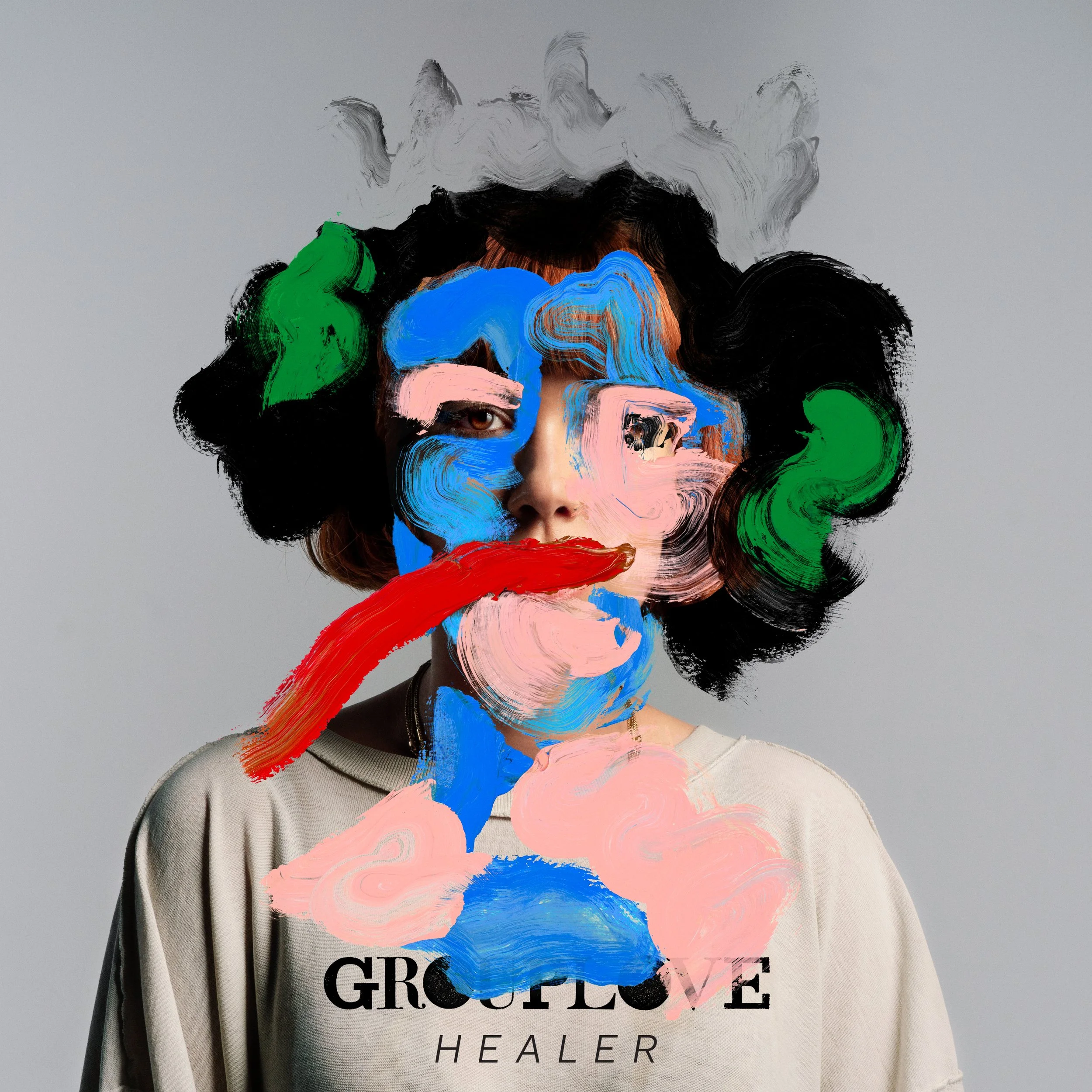 A person with black curly hair wears a beige shirt with the text 'GROUPLOVE HEALER' on it, but the face and hair are obscured by colorful, abstract paint strokes in blue, pink, green, red, and gray, creating an artistic, surreal effect.