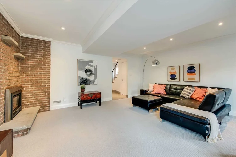 Lower-level family room with an exposed brick fireplace and leather sectional, North Central Toronto, by First Place Homes