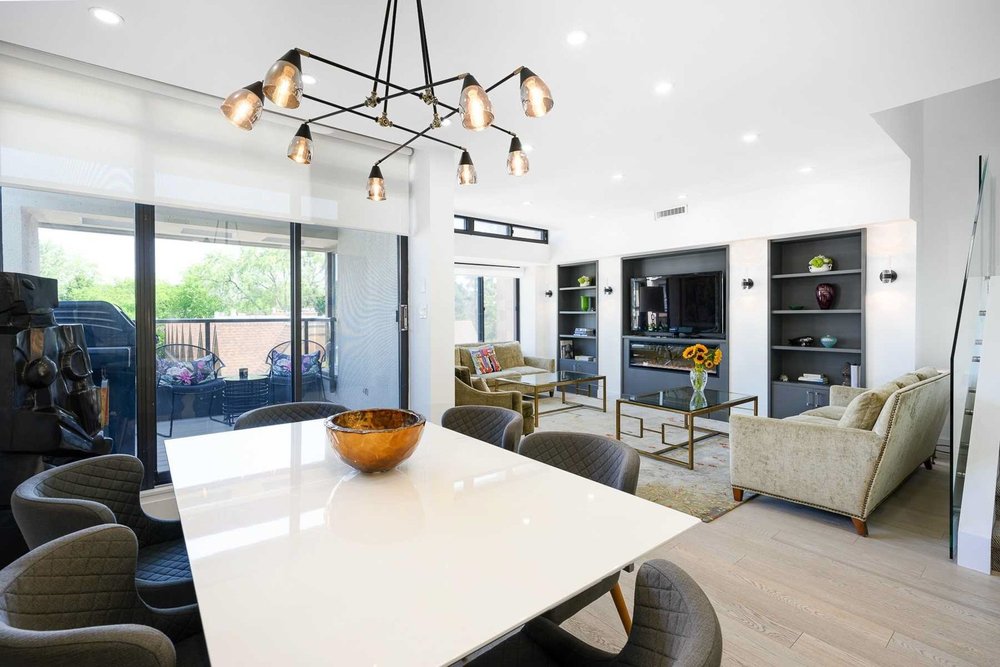 Toronto condominium townhome renovation by First Place Homes: dining table under a chandelier with the living room beyond
