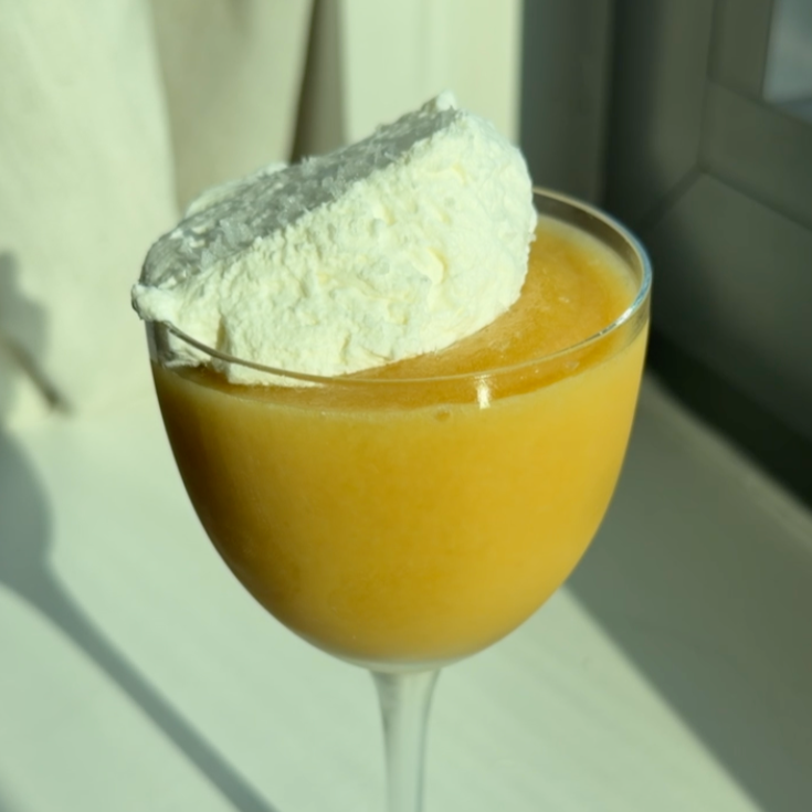 a coupe glass with frozen peach margarita and a salted whip cream